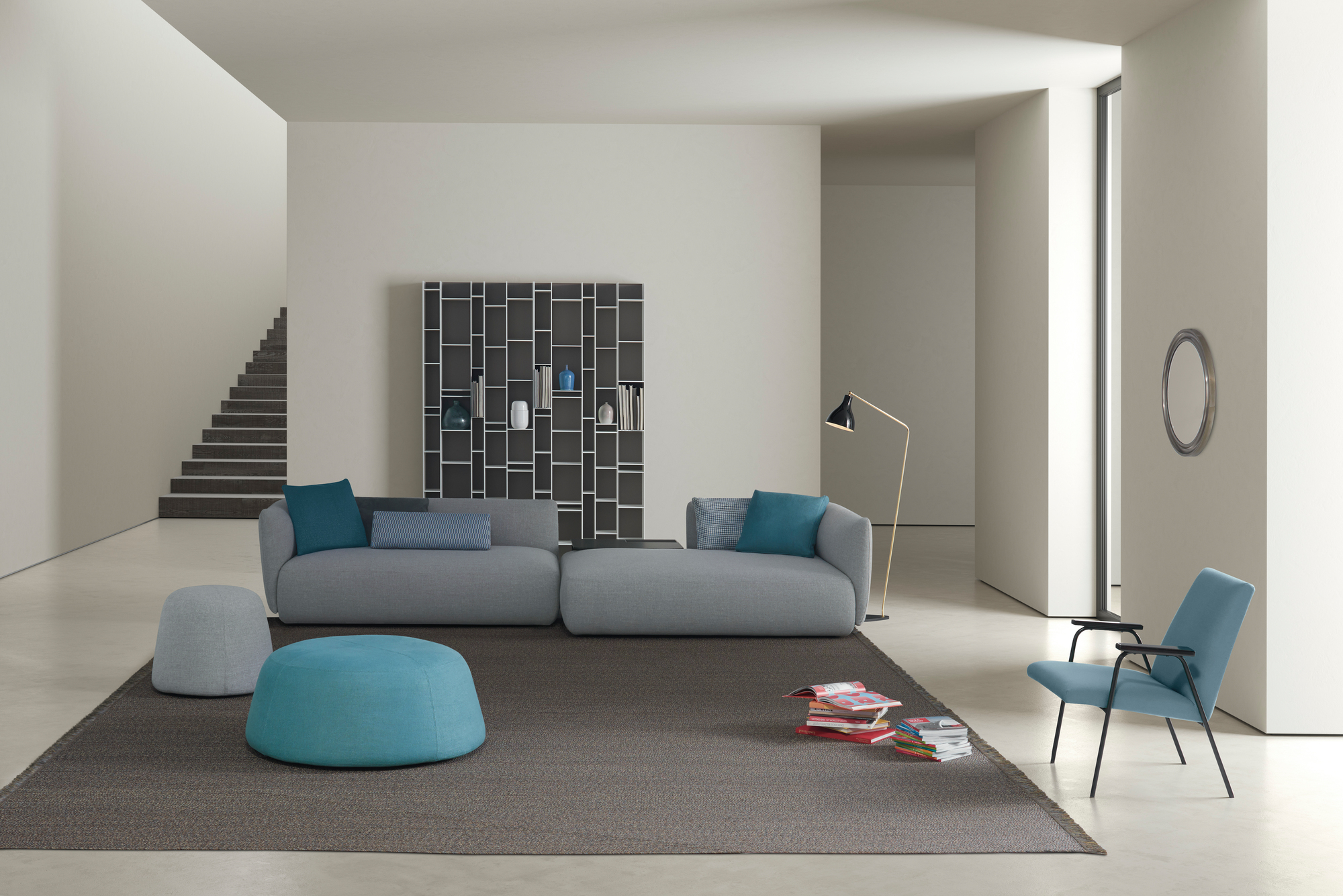 Helles Wohnzimmer mit grauem Cosy Sofa von MDF Italia, blauen Kissen und Poufs.