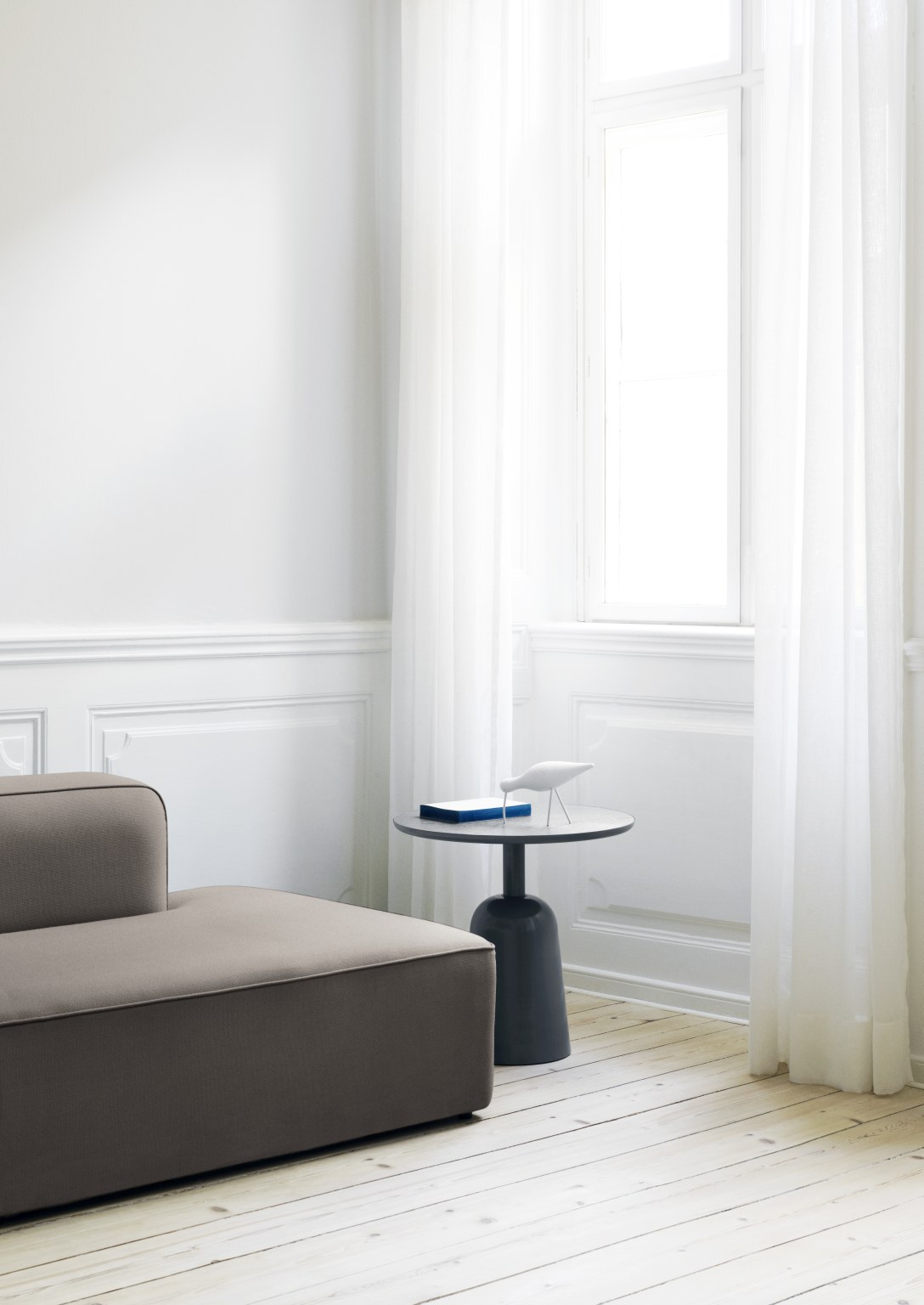 Normann Copenhagen Turn Table Tisch in dunklem Grau neben einem beigen Sofa in hellem Raum.