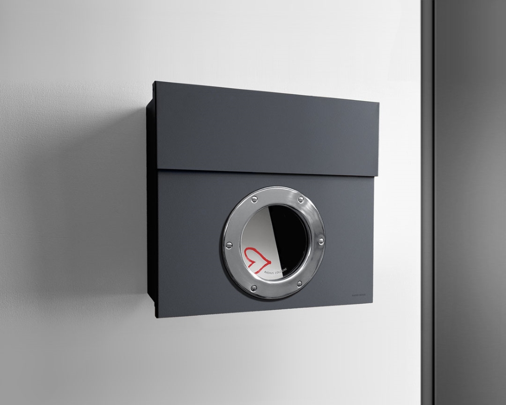 Anthrazitfarbener Letterman Briefkasten mit rundem Sichtfenster aus Edelstahl an einer weißen Wand.
