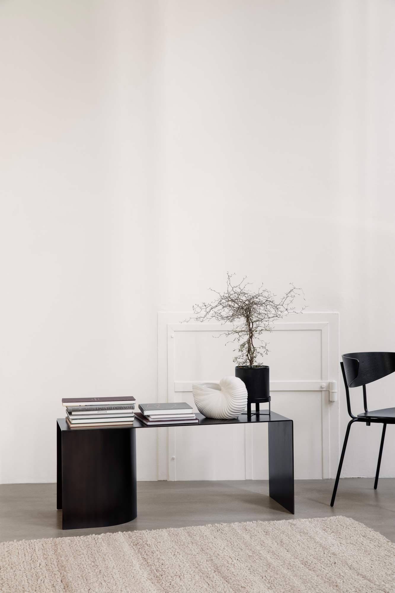 Weiße Ferm Living Shell Pot Vase auf schwarzem Tisch, neben Büchern und Zimmerpflanze.