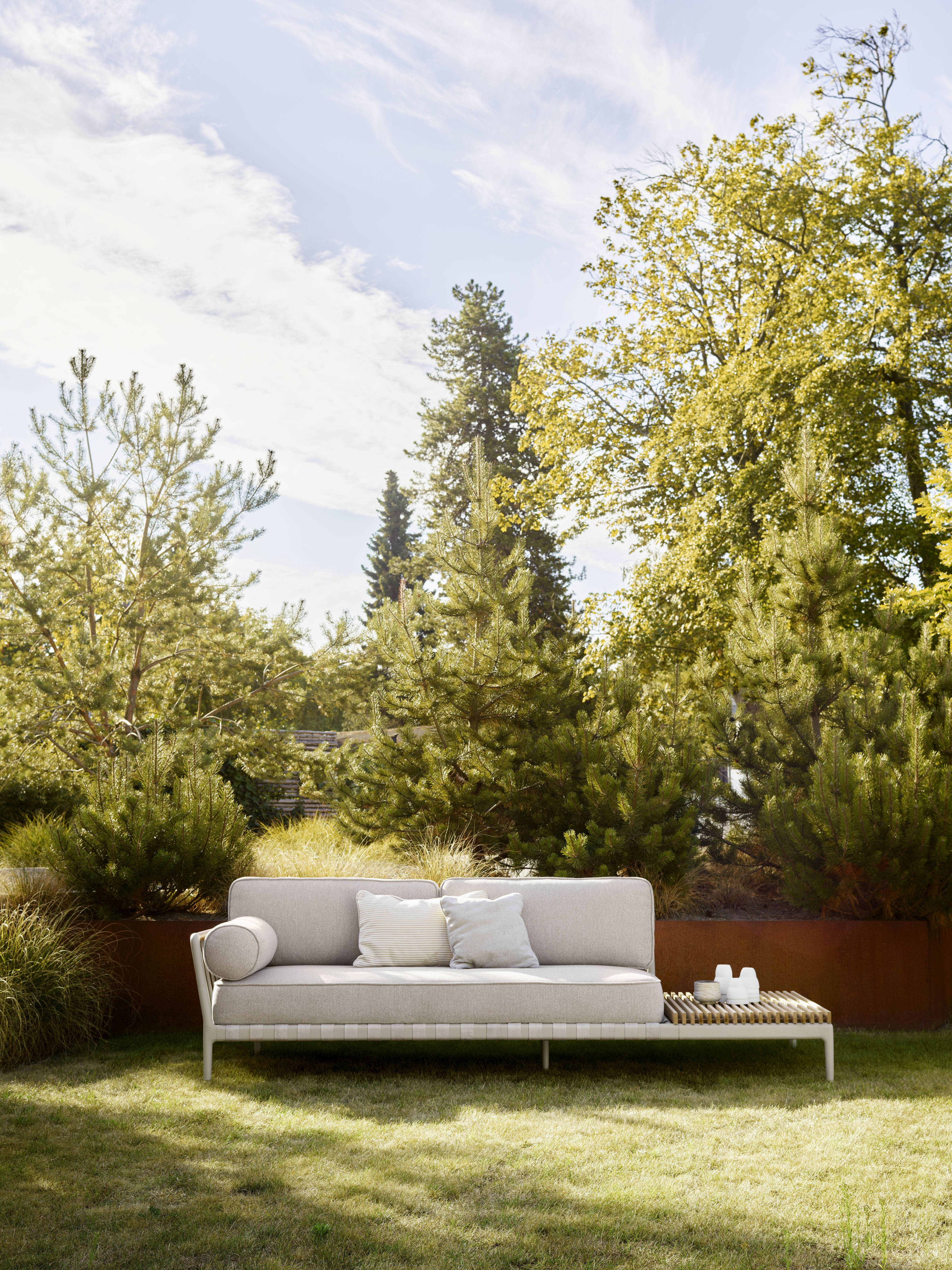 Vipp Open-Air Outdoor Sofa mit offenem Ende links im Garten, helle Polster und Beistelltisch.