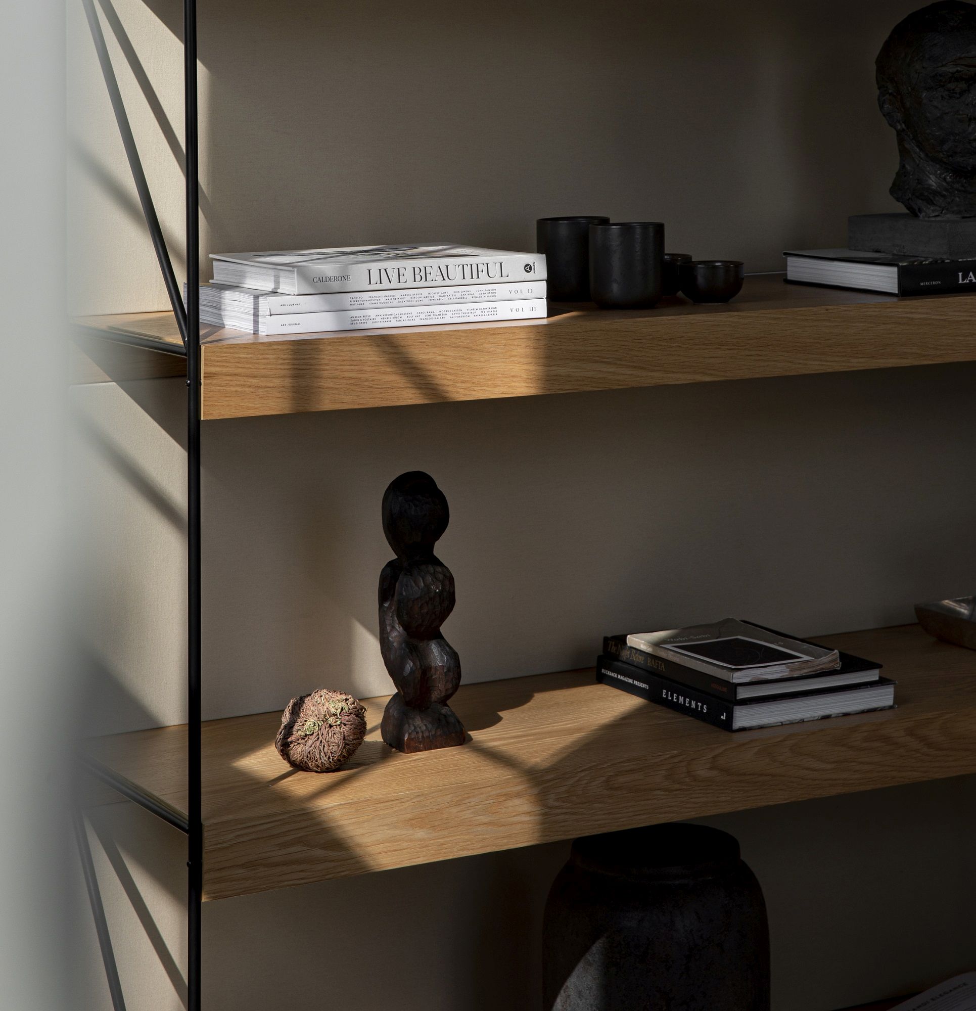 Detailaufnahme des Audo Copenhagen Zet Storage System Regals mit Dekorationselementen und Büchern auf hellen Holzregalböden.