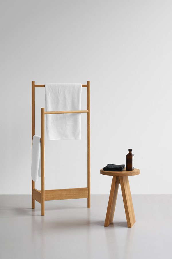 E15 Hocker EK01 aus Holz neben Handtuchhalter mit weißen Handtüchern und Pflegeprodukt.