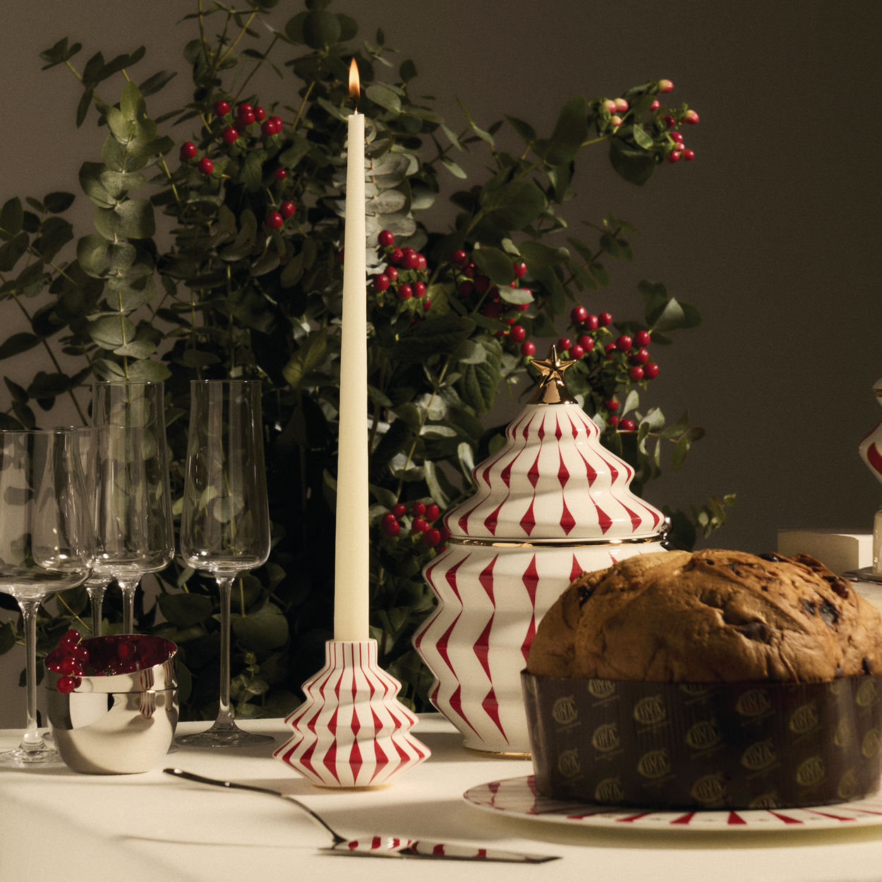 Festliche Tischdekoration mit Alessi Delight Kerzenständer, Panettone, Gläsern und weihnachtlicher Dekoration für ein stimmungsvolles Ambiente.