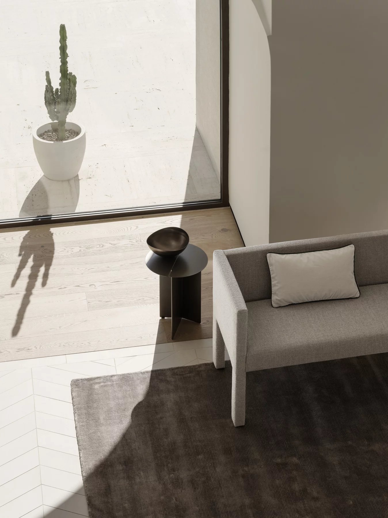 Helle Wohnraum-Szene mit grauem Sitta Sofa, kleinem Beistelltisch, Dekoschale und Teppich von oben.