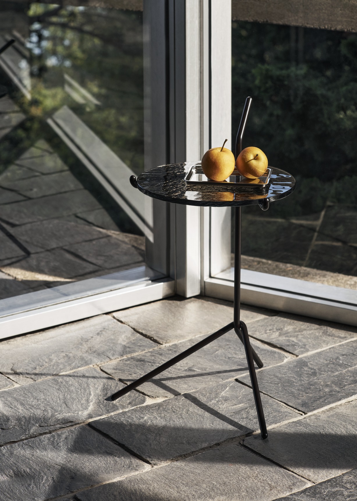 AndTradition Halten SH9 Beistelltisch mit Obst auf Marmorplatte und filigranem, schwarzem Metallgestell.