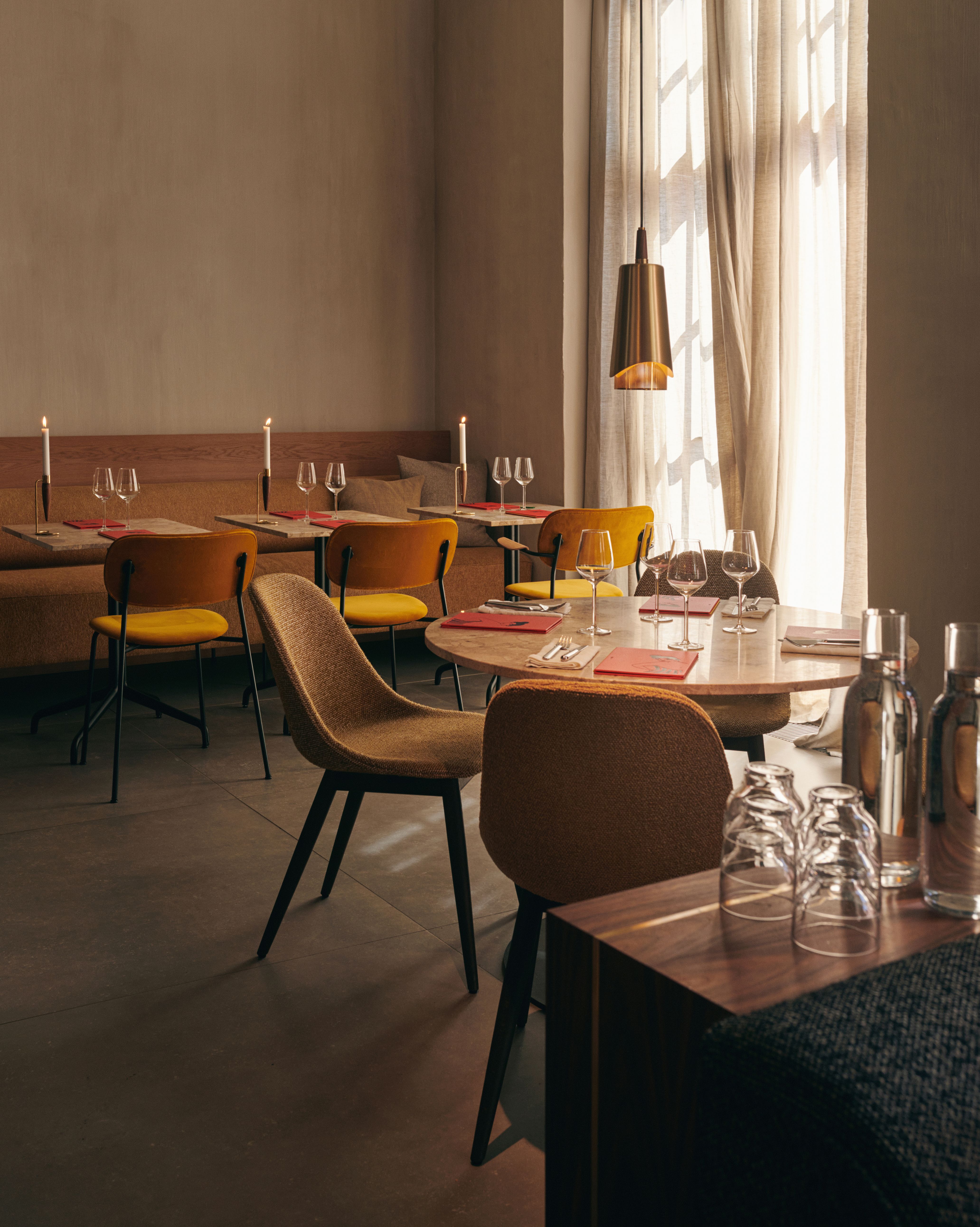 Innenaufnahme eines Restaurants mit Tischen, Stühlen und der goldenen Umanoff Hängeleuchte von Audo über einem Tisch.