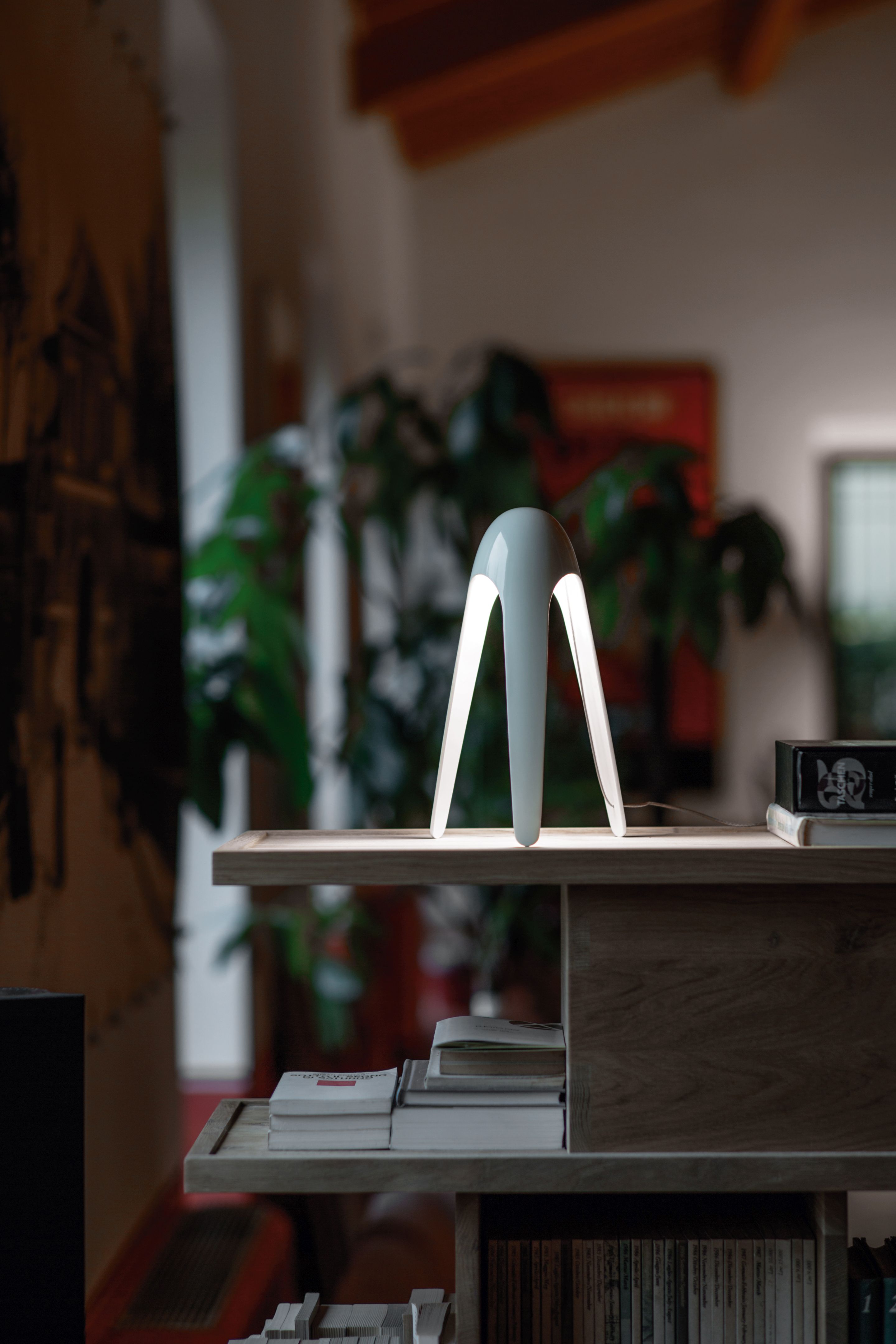 Weiße Cyborg Tischleuchte von Martinelli Luce auf einem Holzregal mit Büchern im Hintergrund.