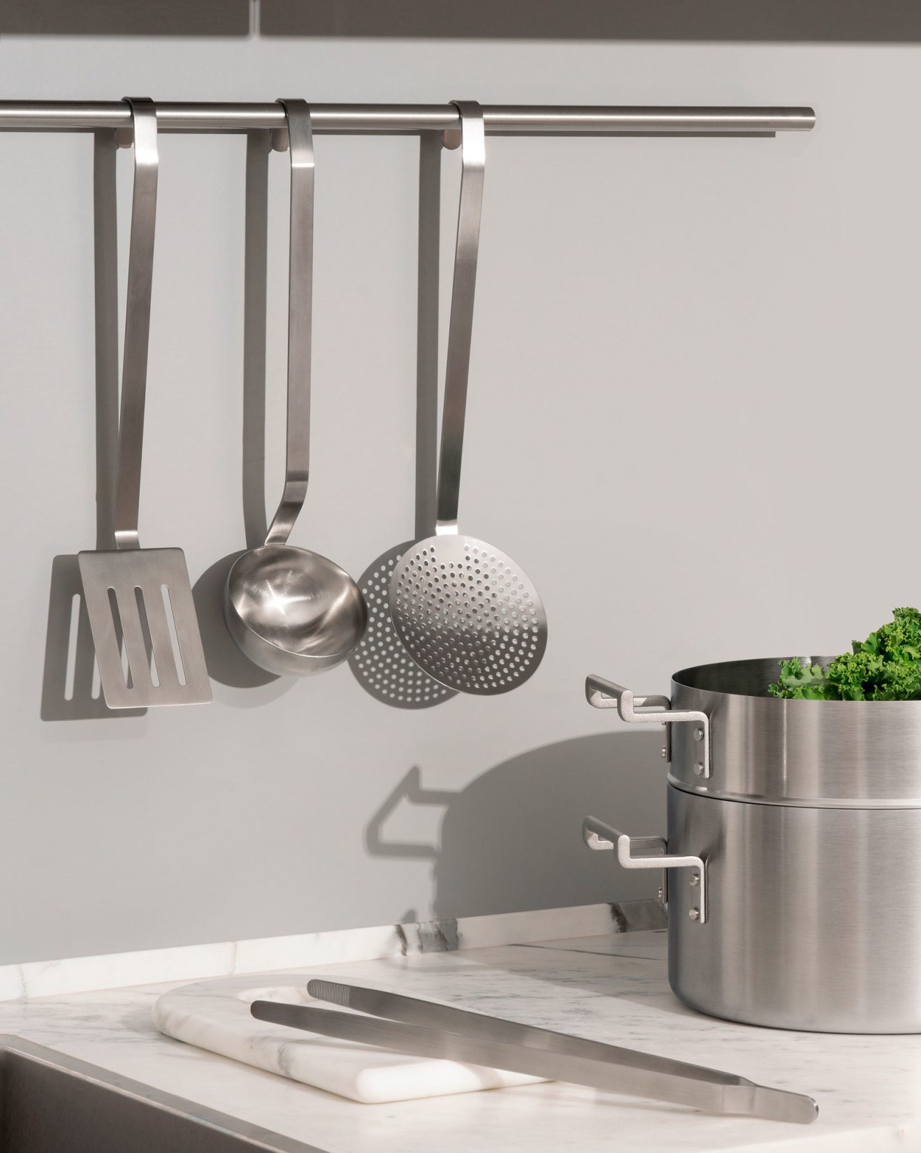 Alessi Convivio Küchenset: Edelstahl Kochutensilien mit Pfannenwender, Schöpfkelle, Schaumlöffel, Kochtopf und Küchenzange auf Marmor Arbeitsplatte.