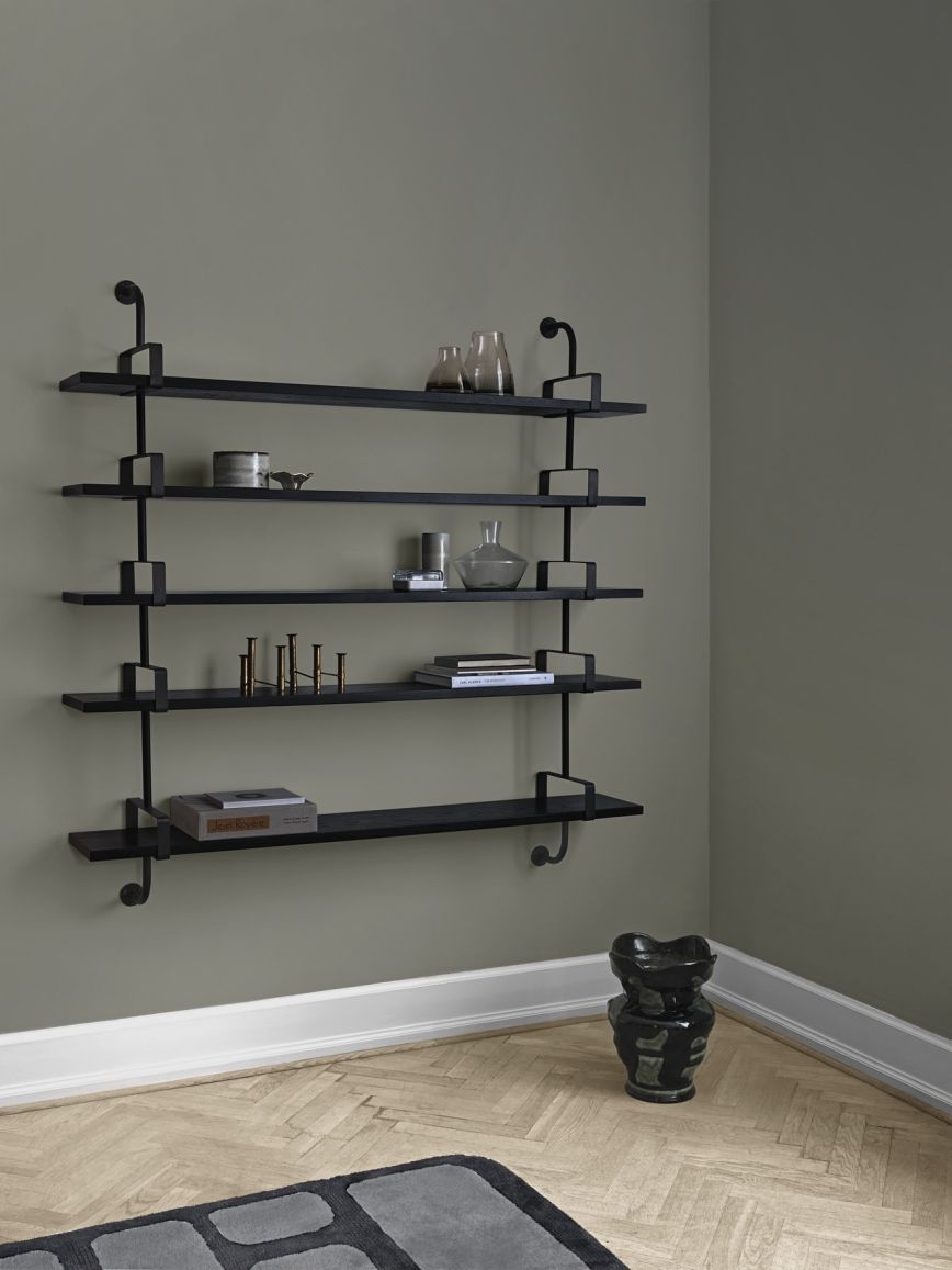 Schwarzes Démon Regal von Gubi an einer Wand, dekoriert mit Büchern und Vasen.