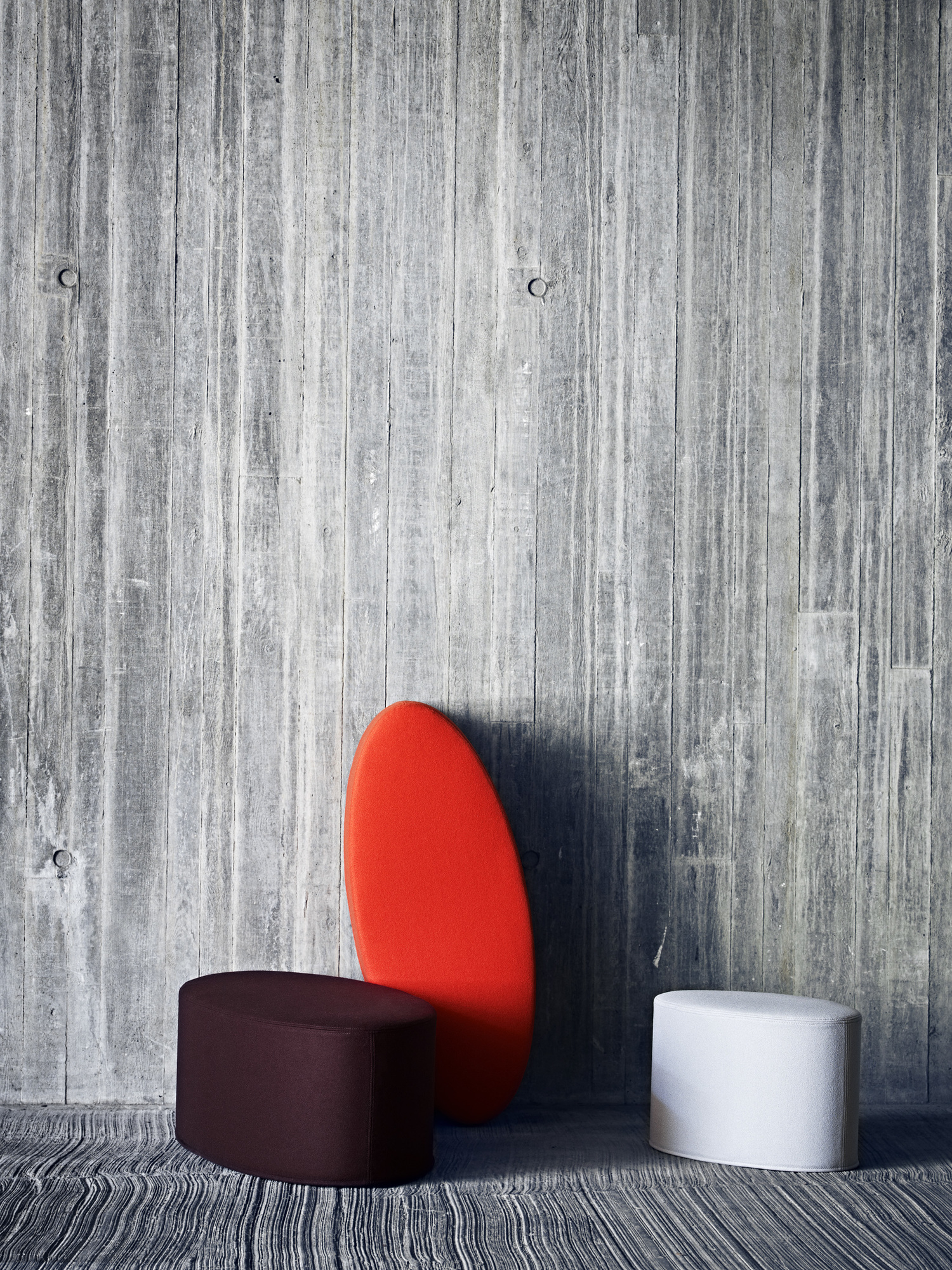 Bon Bon Hocker in Braun, Weiß und Rot vor einer Betonwand, moderne Sitzmöbel für Wohnzimmer.