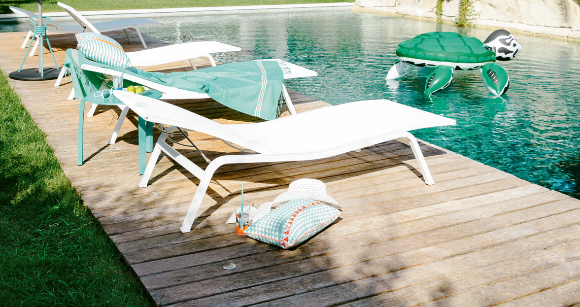 Weiße Alizé Sonnenliege von Fermob am Pool auf Holzdeck mit Dekoration und aufblasbarer Schildkröte.