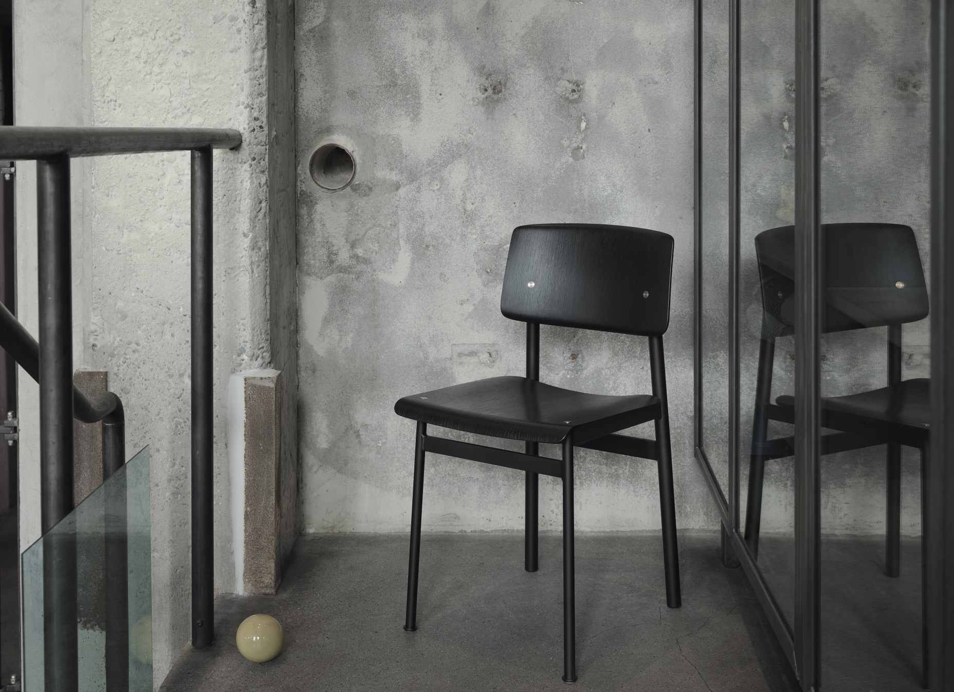Schwarzer Loft Chair Stuhl von Muuto vor einer Betonwand, minimalistisches Design, skandinavische Möbel.