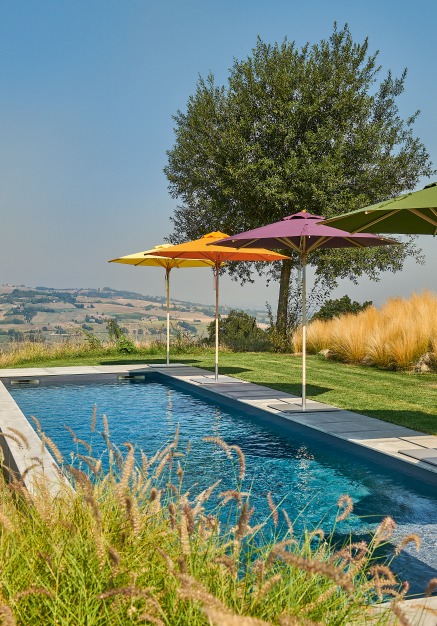 Weishäupl Klassiker Sonnenschirme in Gelb, Orange, Lila und Grün am Pool mit malerischer Landschaft im Hintergrund.