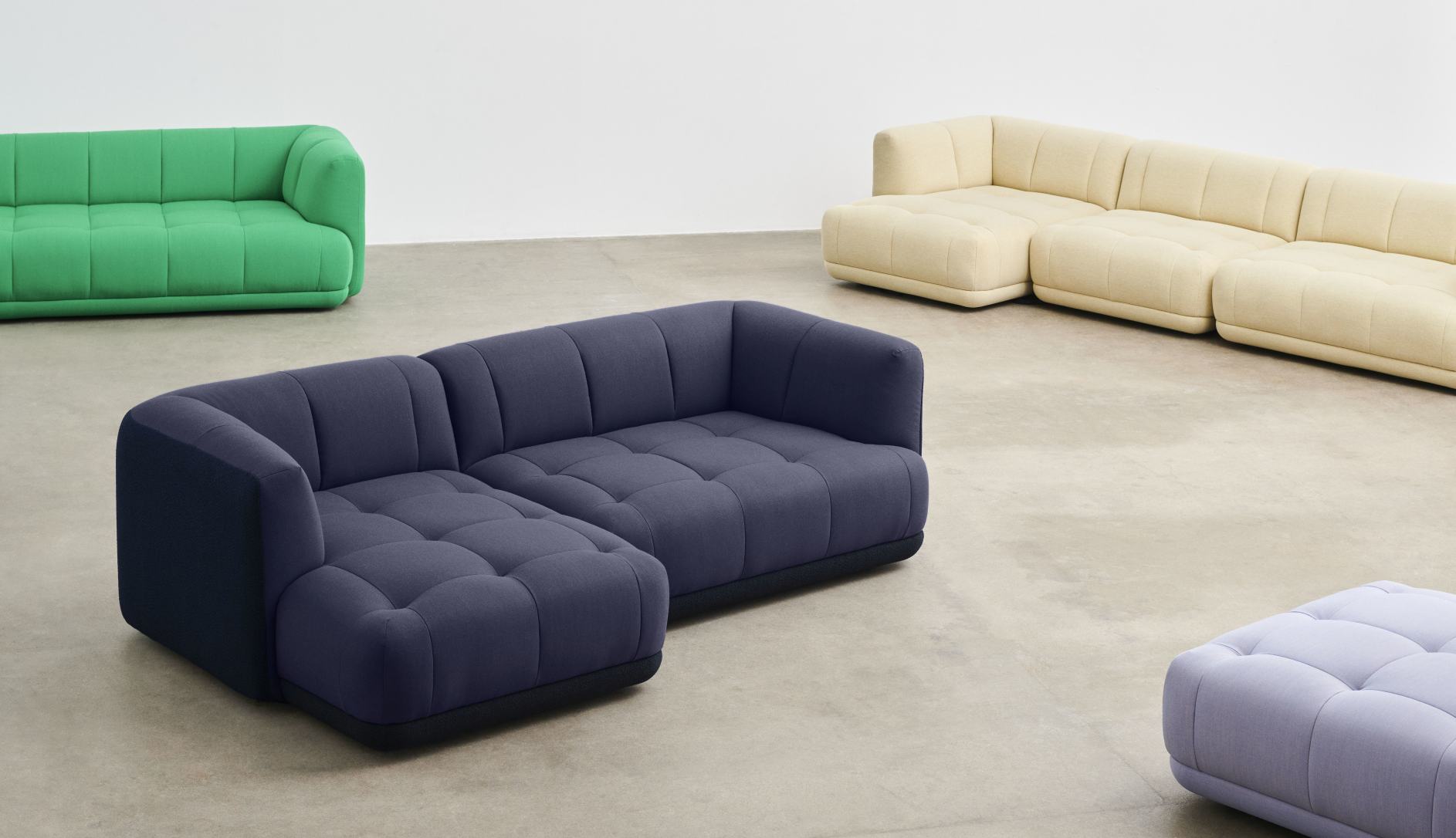 Blaues Quilton Sofa von Hay mit Ottomane und weiteren Sofas in Grün und Beige.