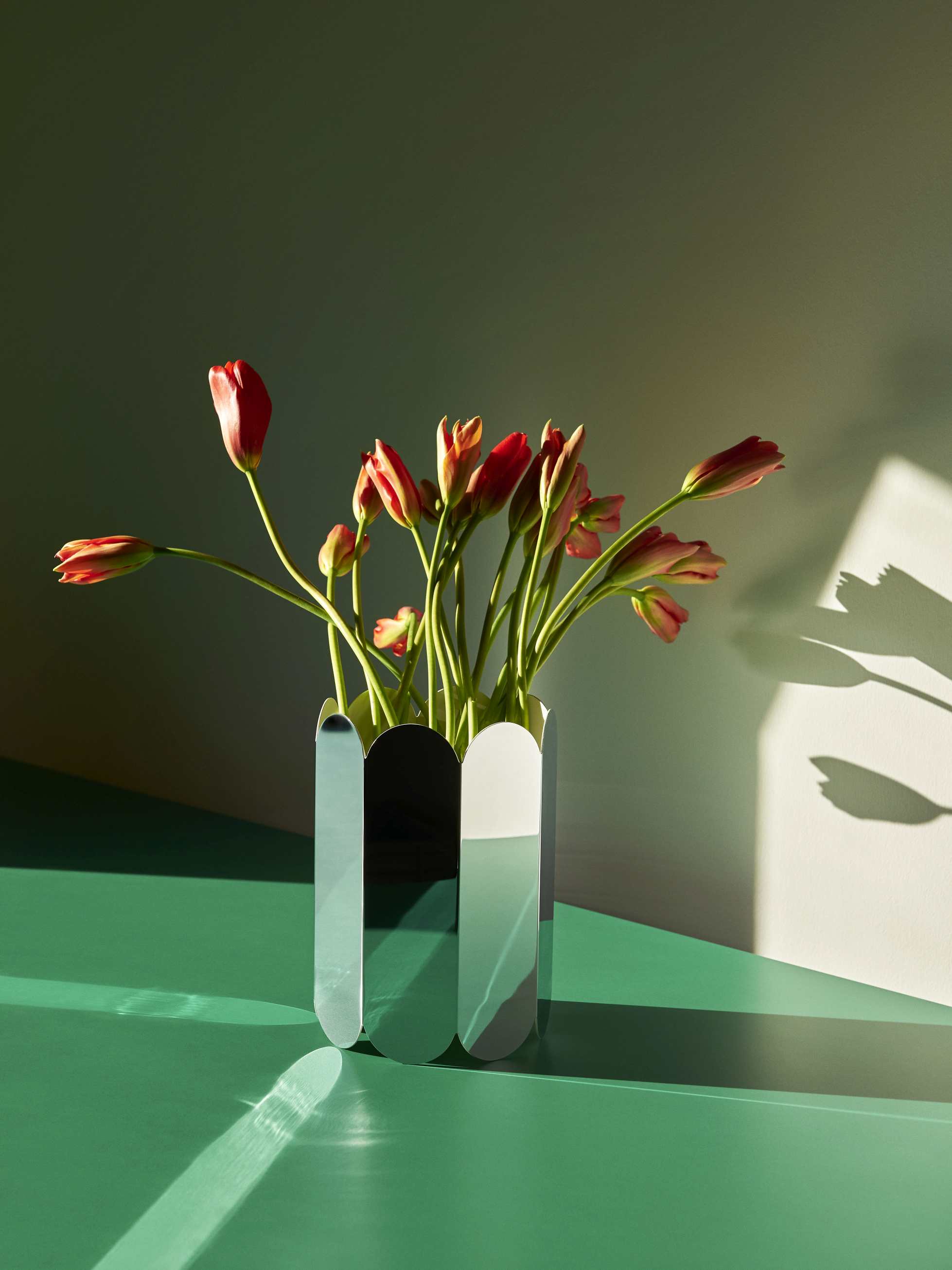 Nahaufnahme der Hay Arcs Vase L Mirror mit roten Tulpen auf einem grünen Tisch.