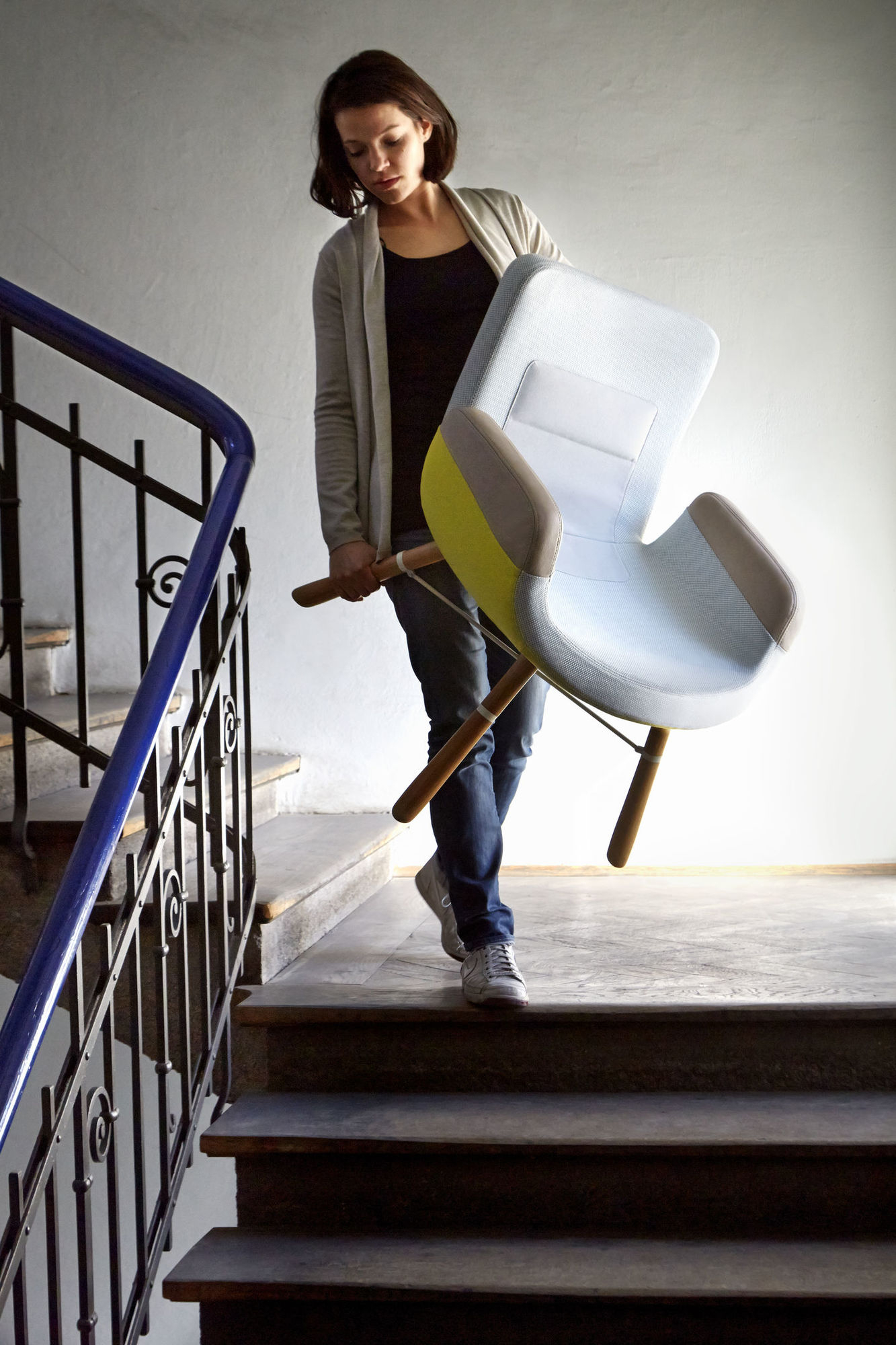 Frau trägt East River Chair Sessel von Vitra die Treppe hinunter, hellblau mit gelben Akzenten.