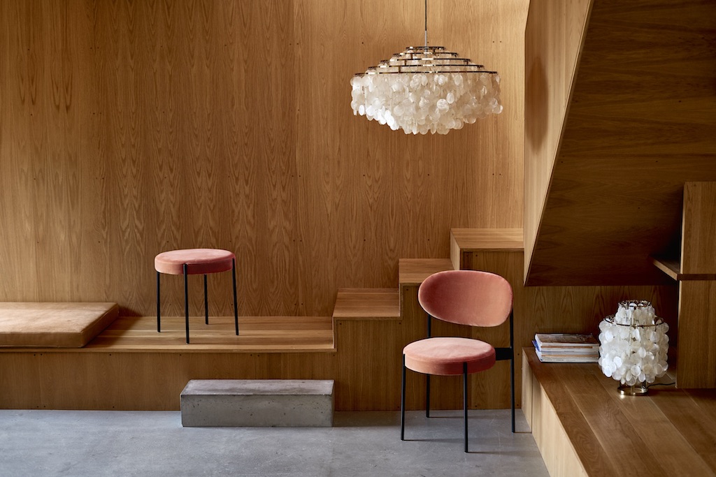 Verpan Series 430 Hocker in Rosa mit schwarzem Gestell vor Holzwand und Design-Leuchten.