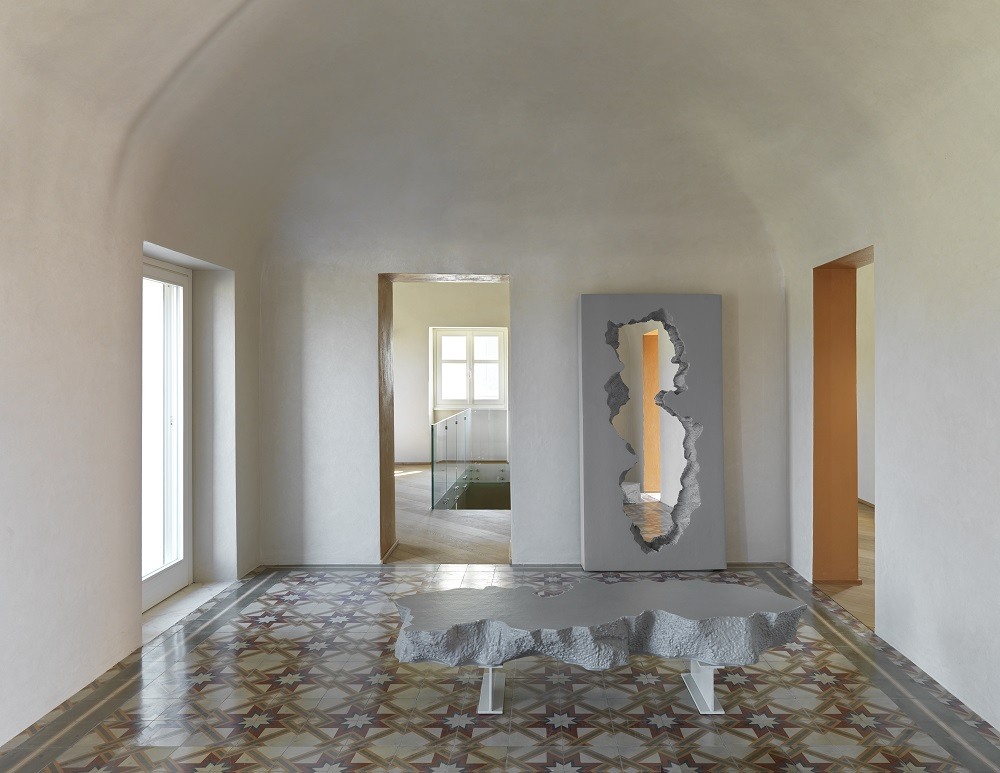 Innenaufnahme mit Gufram Spiegel "Broken Mirror" und passendem Tisch in grauem Design.