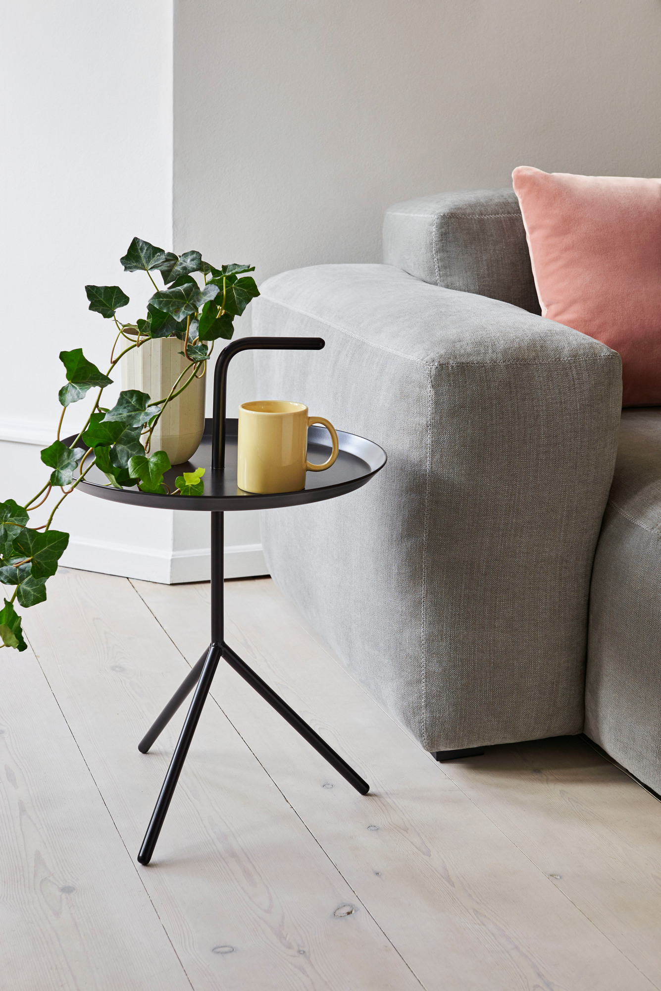 Schwarzer Hay DLM Beistelltisch mit Pflanze und gelber Tasse neben einem grauen Sofa.