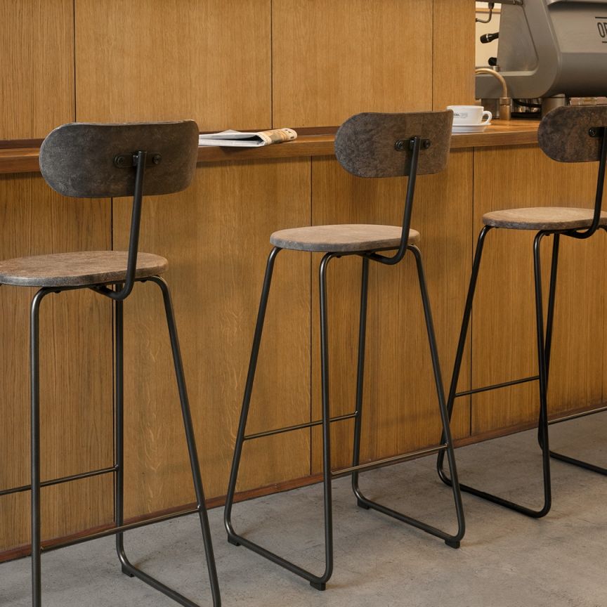 Drei moderne Barhocker mit Rückenlehne und schwarzem Metallgestell vor einer Holzwand.