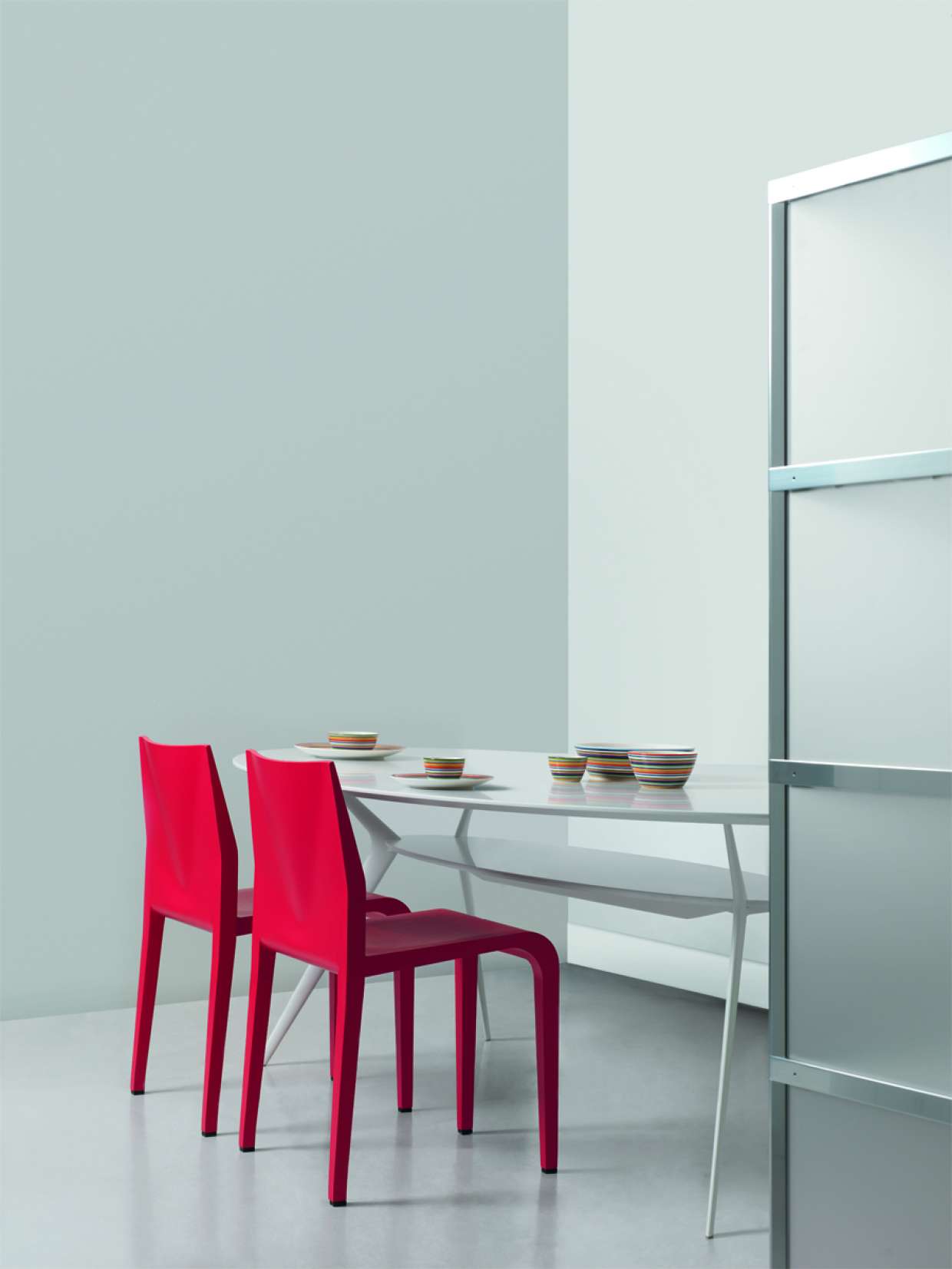 Zwei rote Laleggera Stühle von Alias an einem Esstisch mit Geschirr in minimalistischem Interieur.
