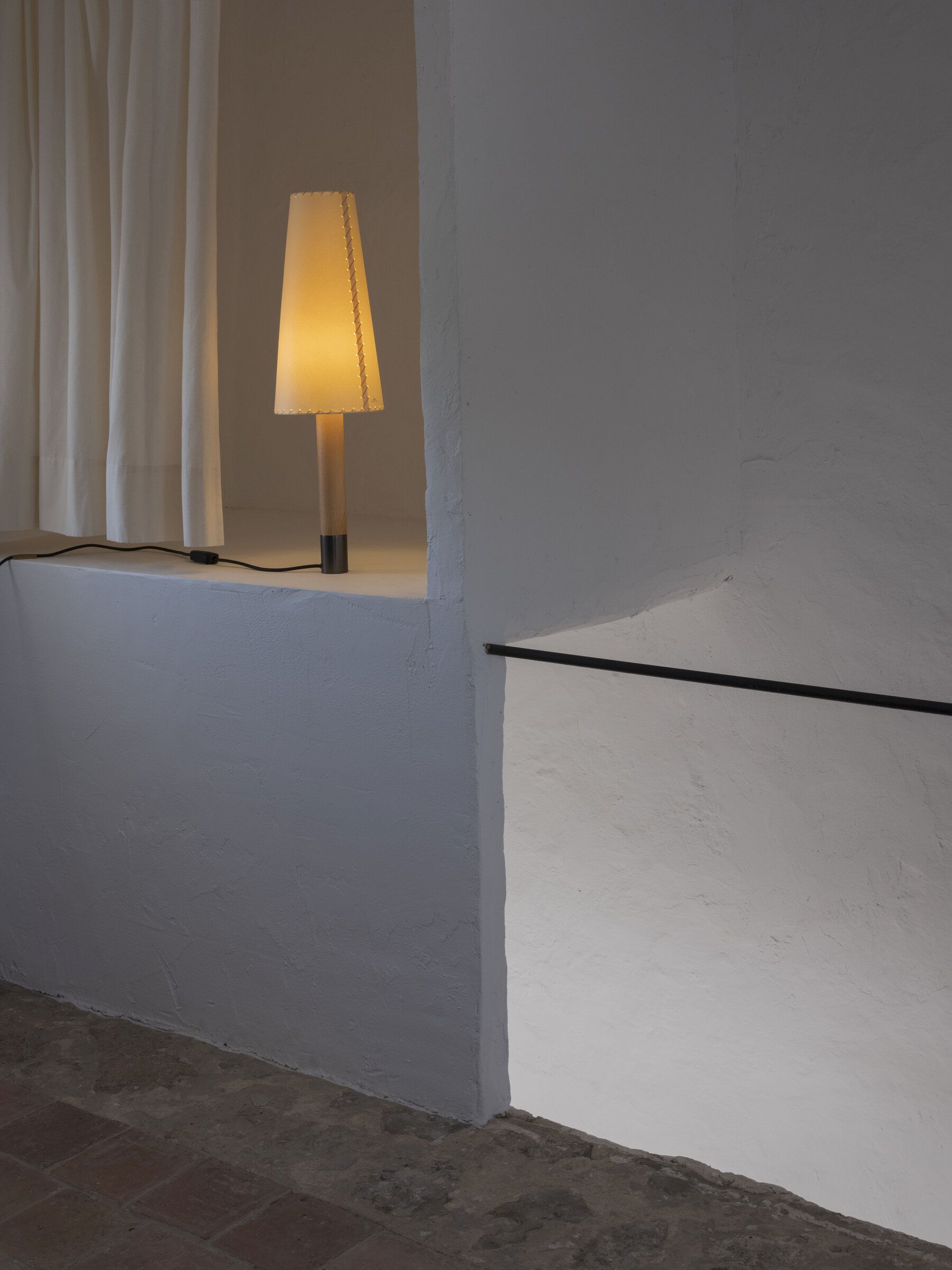 Nahaufnahme der Basica Tischleuchte von Santa & Cole, die warmes Licht in einem minimalistischen Raum spendet.