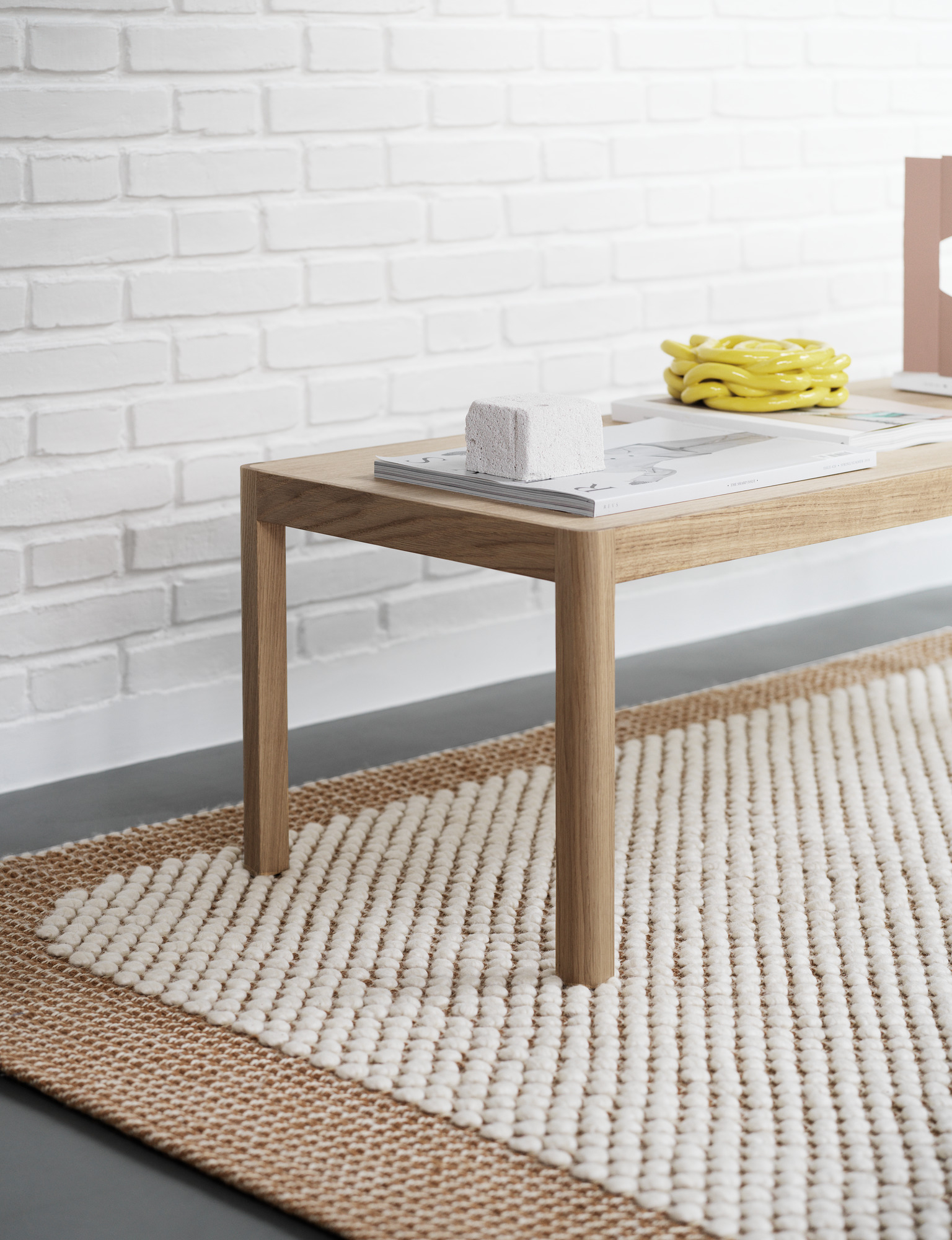 Muuto Workshop Couchtisch aus Eichenholz auf einem Teppich vor einer weißen Ziegelwand.