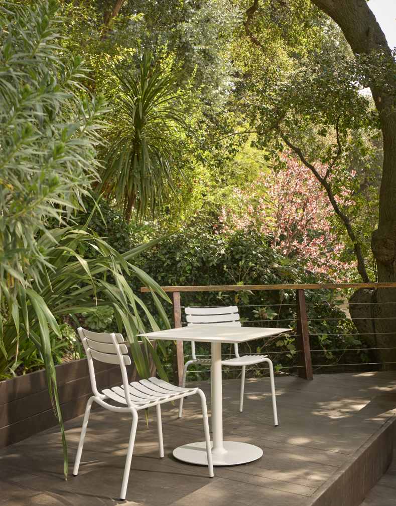 Alua Dining Chair von Houe, weiße Gartenstühle und Tisch auf einer Holzterrasse im Grünen.