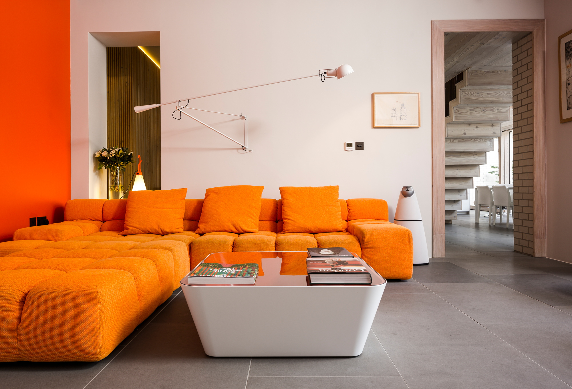 Wohnzimmer mit orangefarbenem Sofa und weißer Flos Wandleuchte, verstellbare Lampe für Innenbeleuchtung.