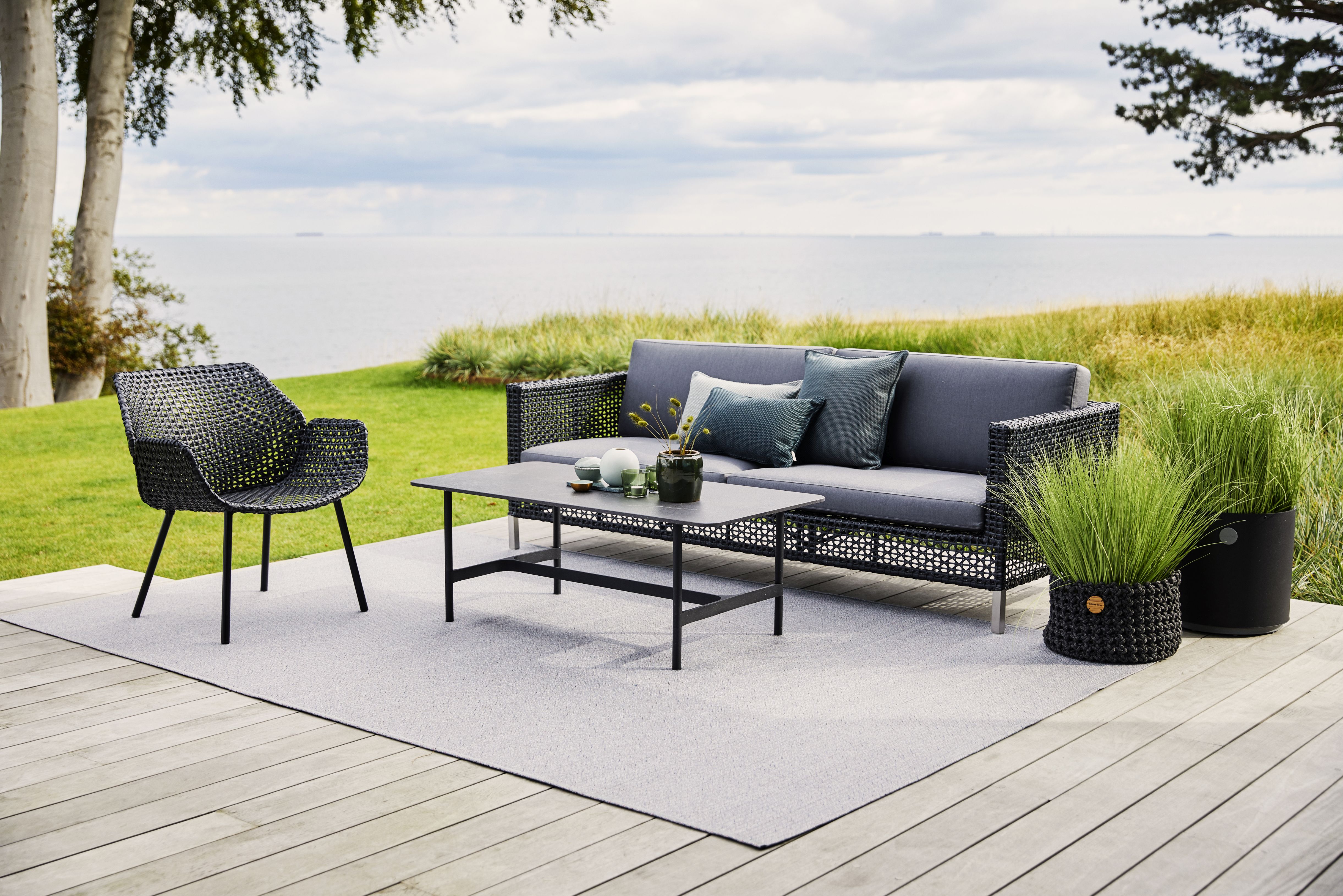 Dot Outdoor Teppich Ø200 cm von Cane-Line auf einer Terrasse mit Gartenmöbeln und Meerblick.