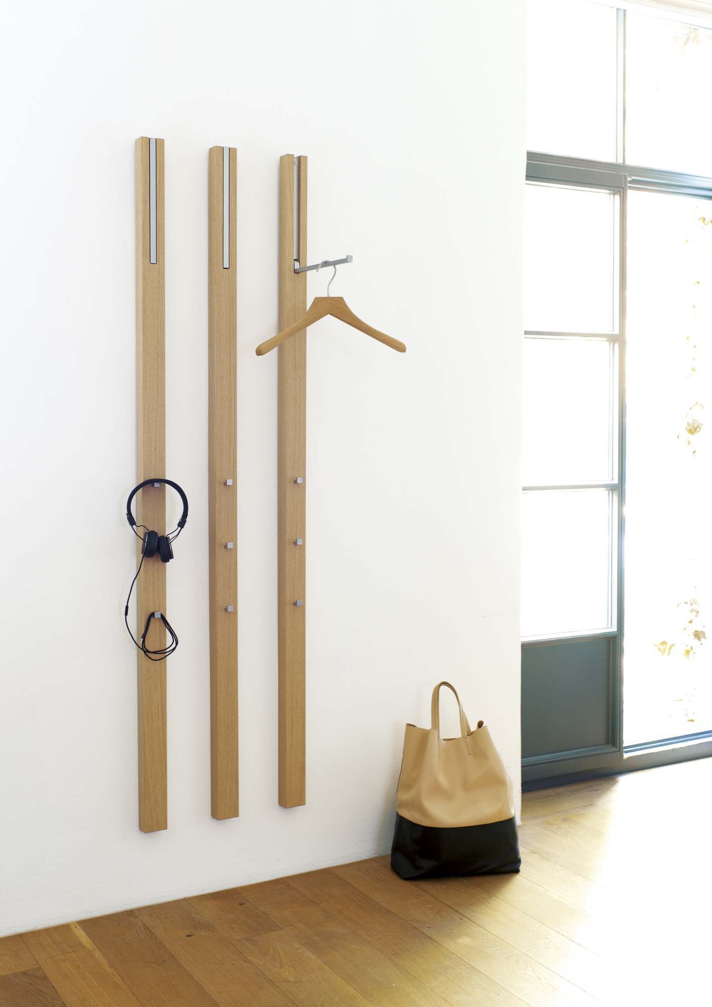 Schönbuch 0112 Garderobenpaneel aus Holz mit Kleiderbügel, Kopfhörer und Tasche an einer weißen Wand.