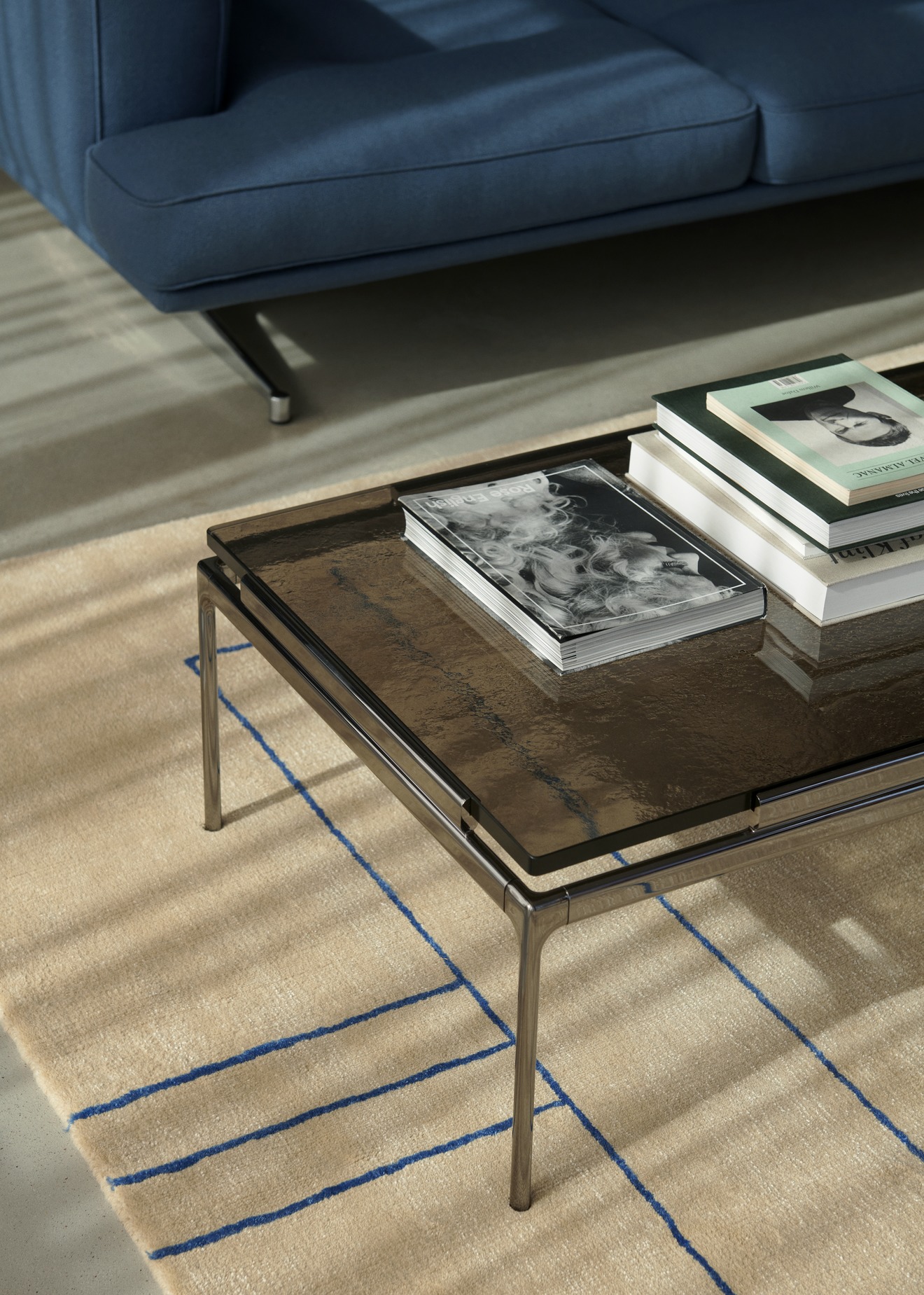 AndTradition Cruise Teppich AP11 mit blauem Linienmuster unter einem Couchtisch in Wohnzimmer-Szene.