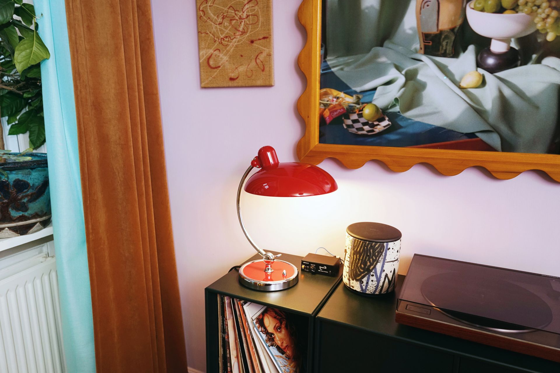 Rote Schreibtischlampe im Retro-Design auf schwarzem Regal mit Schallplattenspieler und Lautsprecher im Wohnzimmer.