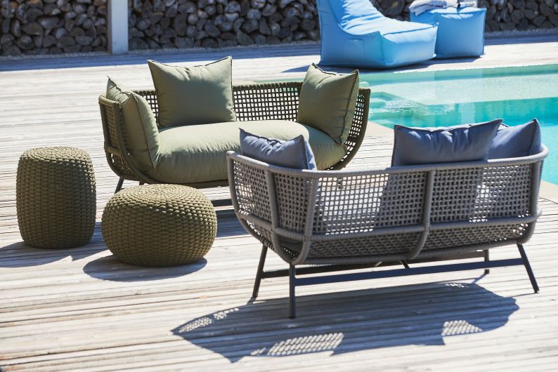 Hellgraues Suka Loungesofa von Jan Kurtz mit Outdoor-Kissen und Poufs auf einer Holzterrasse.