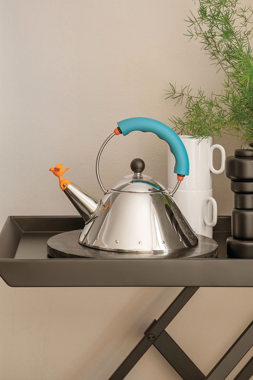 Alessi Wasserkessel 9093/1 LAZ aus Edelstahl mit blauem Griff und Vogelpfeife auf einem Tablett.