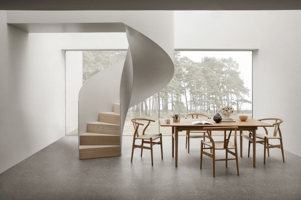 Esszimmer mit Teak-Esstisch und sechs CH24 Wishbone Stühlen von Carl Hansen & Søn vor Fenster und Wendeltreppe.