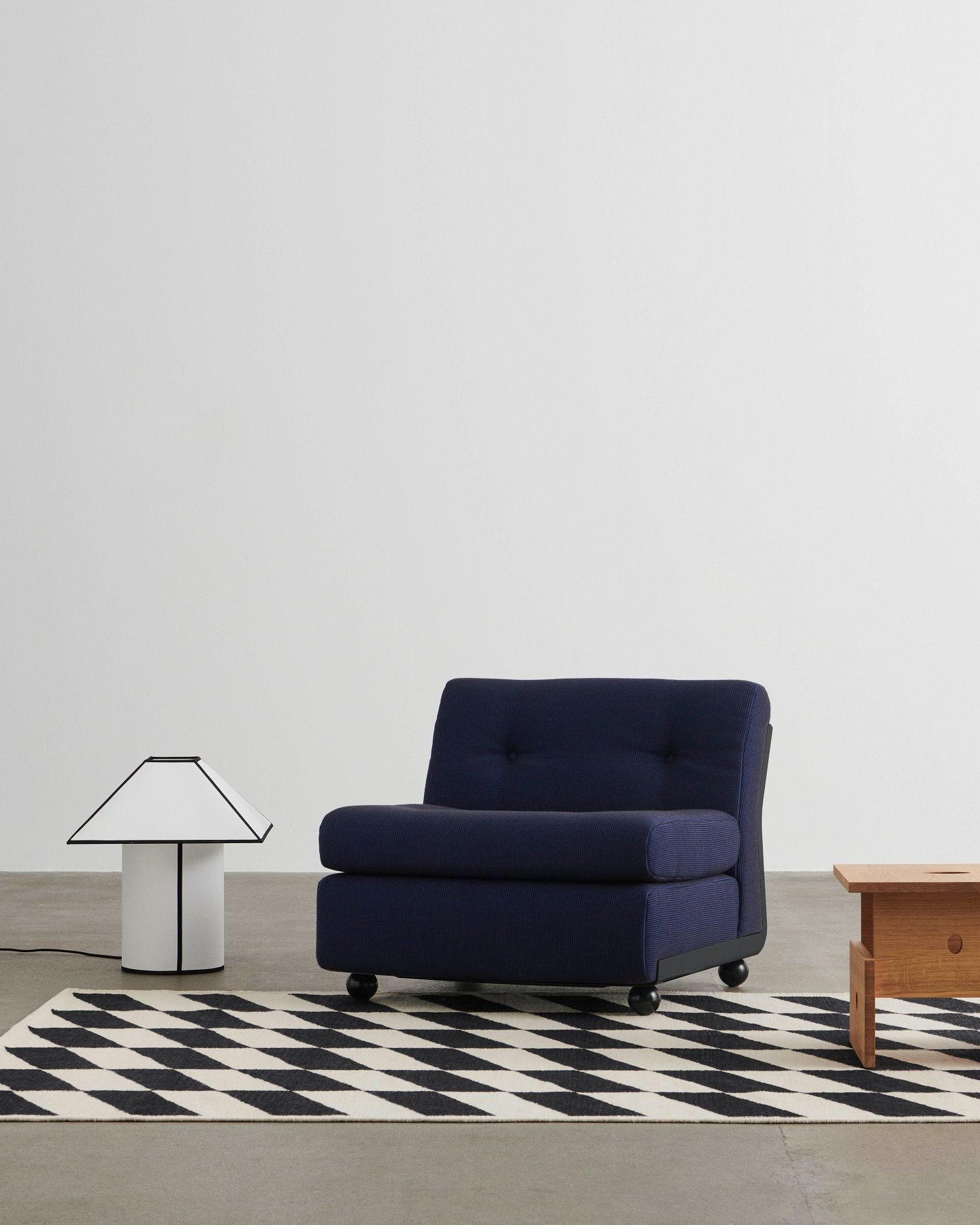 Ava Pyramid Table Lamp von Hay neben Sessel und Teppich im minimalistischen Wohnzimmer.
