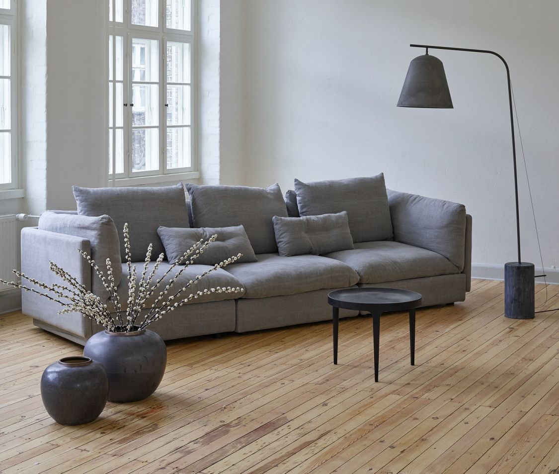 Graues modulares Sofa mit Kissen, Beistelltisch und Stehlampe in einem hellen Wohnzimmer.