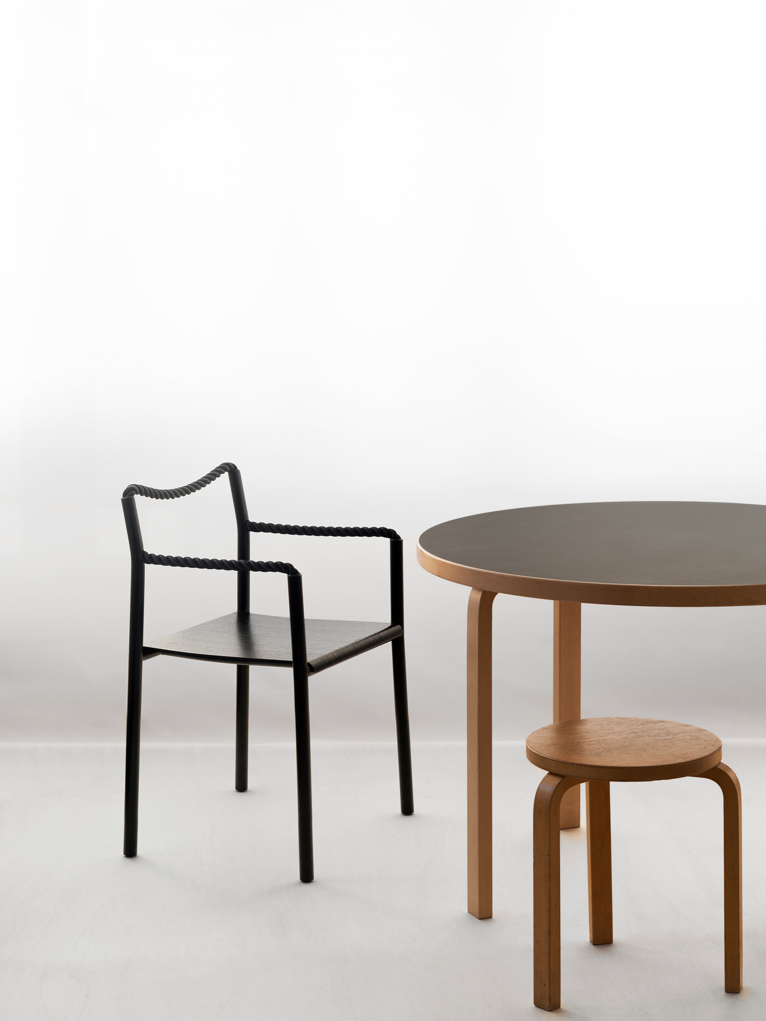 Artek Rope Chair Stuhl mit schwarzem Gestell, Holztisch und Hocker auf weißem Hintergrund.
