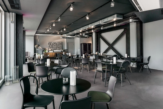 Innenaufnahme eines Restaurants mit schwarzen Vitra Belleville Tischen und Stühlen auf dunklem Boden.