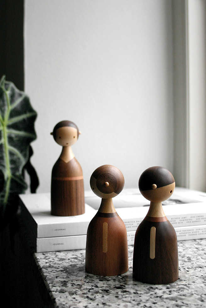 Drei Architectmade Holzfiguren, Kin Baby, auf einem Tisch vor einem Fenster. Dekorative Holzobjekte.
