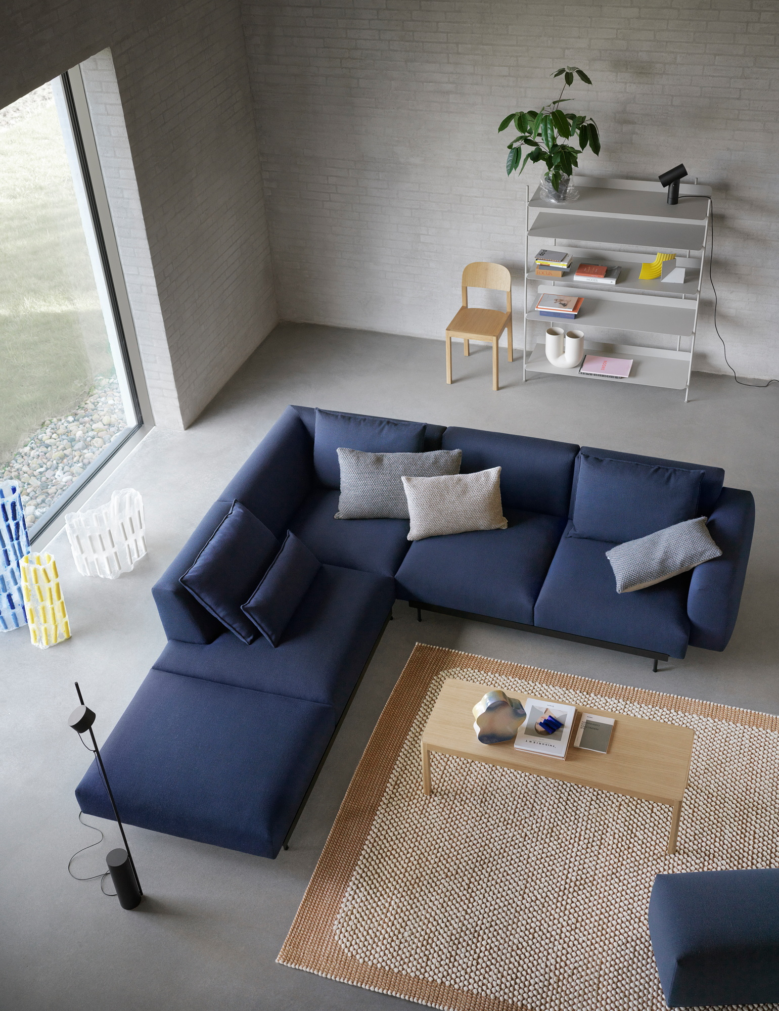 Helle Wohnung mit blauem Ecksofa, Holztisch auf Teppich und Muuto Compile Regalsystem mit verschiedenen Höhen.