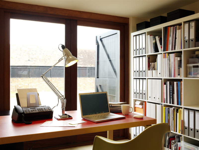 Modernes Homeoffice mit Schreibtisch, Laptop, Schreibtischlampe, Regal und Fenster für konzentriertes Arbeiten.