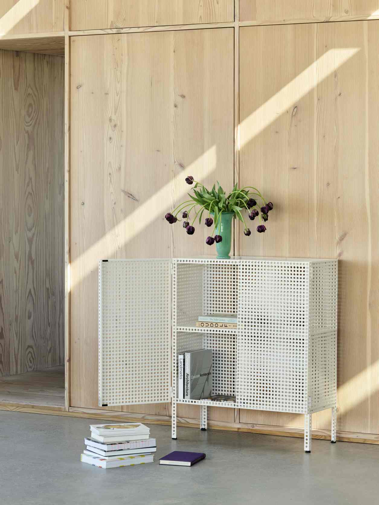 Weißes Hay Sideboard "Perforated Cabinet Floor" mit Lochmuster, Bücher und Vase im modernen Wohnzimmer.