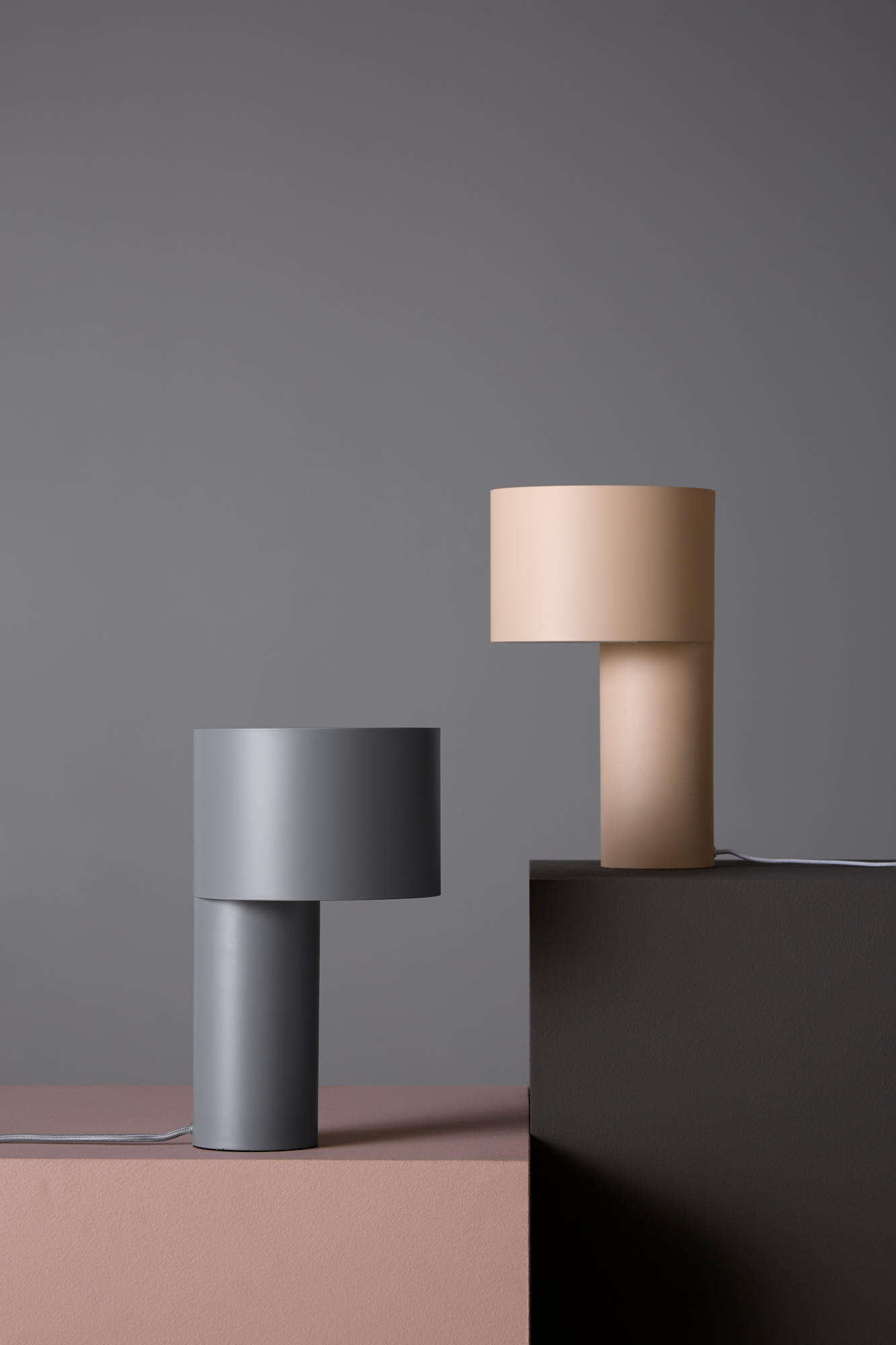 Zwei moderne Tangent Tischleuchten von Woud in Grau und Beige auf farbigen Podesten.