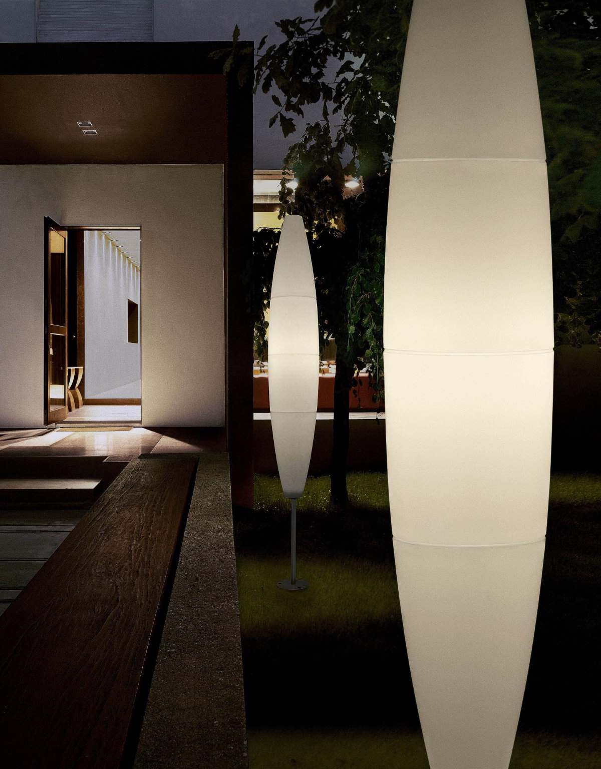 Havana Outdoor Stehleuchte von Foscarini: Zwei weiße, leuchtende Outdoor-Lampen im Garten.