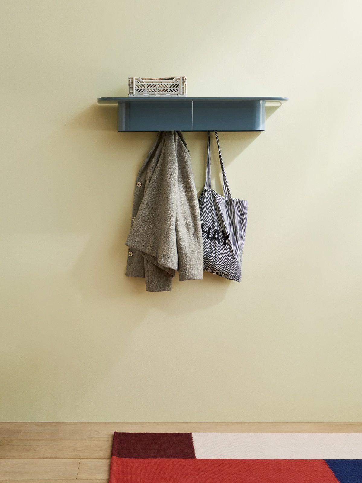 Blaues Hay Korpus Shelf Wandregal mit vier Haken, daran hängen Jacke und Tasche.