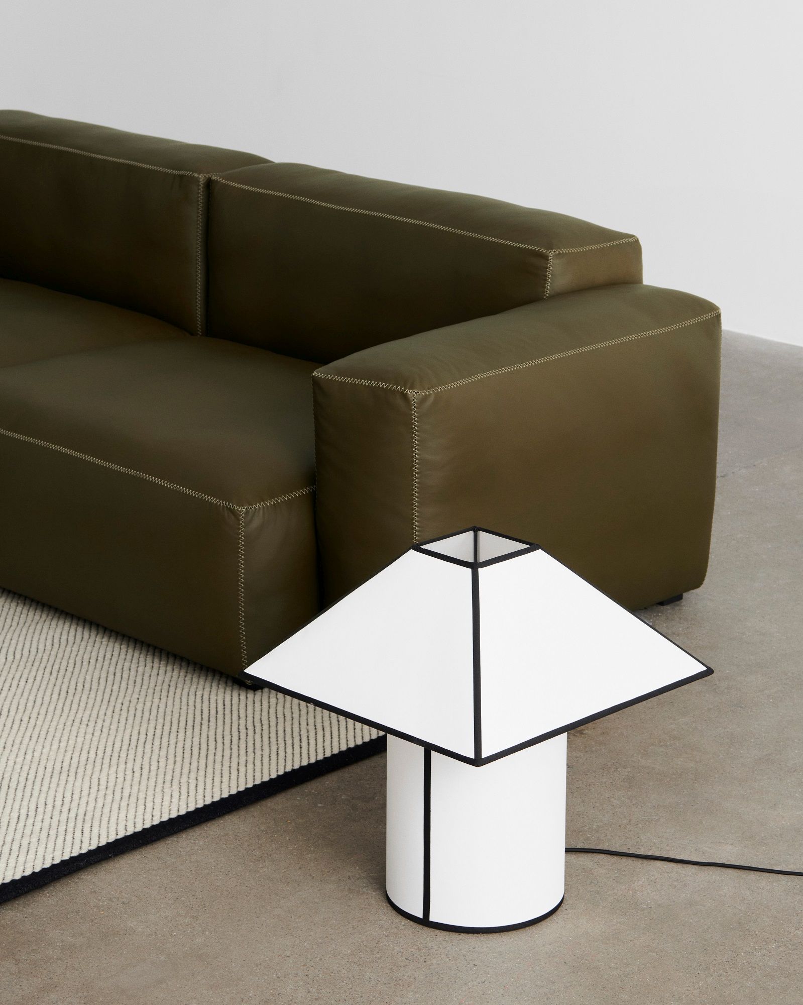 Nahaufnahme der modernen Hay Ava Pyramid Tischleuchte in Weiß und Schwarz neben einem grünen Sofa.