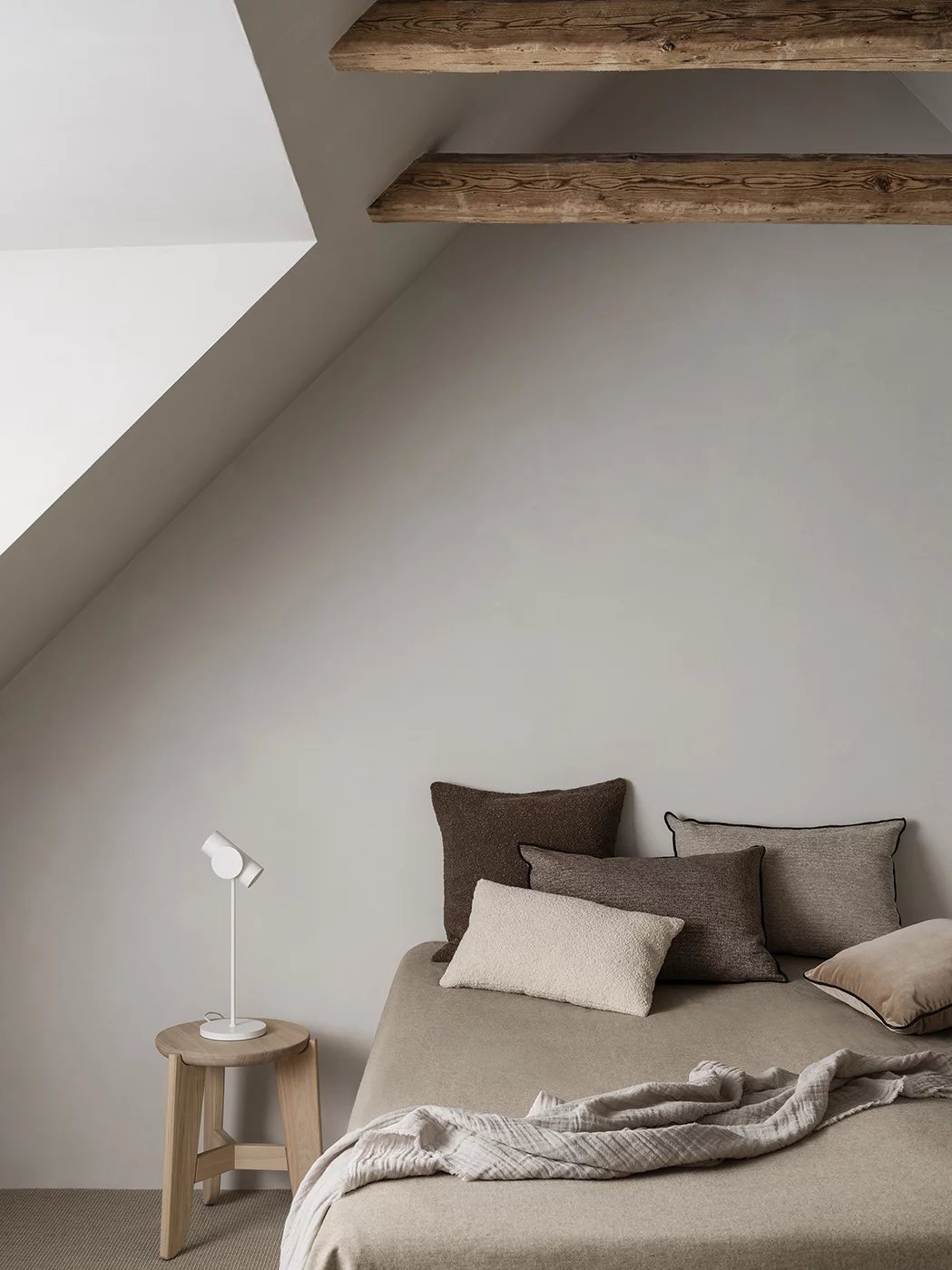 Eli Stool Sitzhocker von Blomus neben Bett mit Kissen und Lampe im Schlafzimmer.